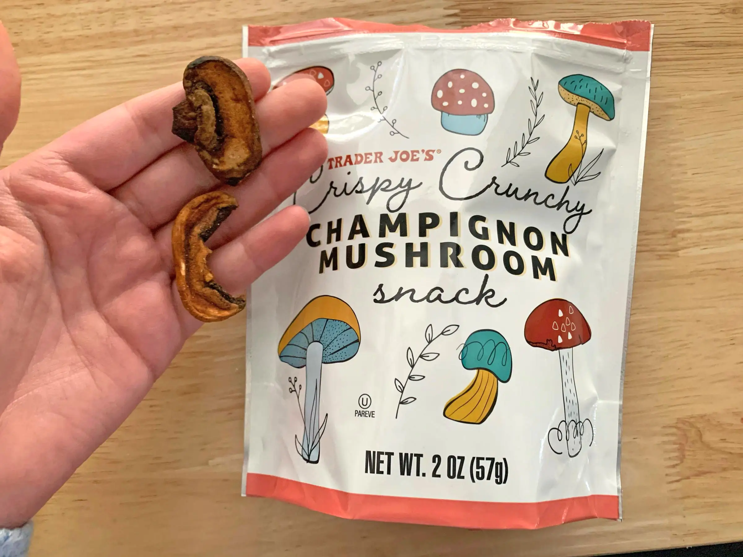 A hand holding a crispy mushroom next to the bag the product came in.