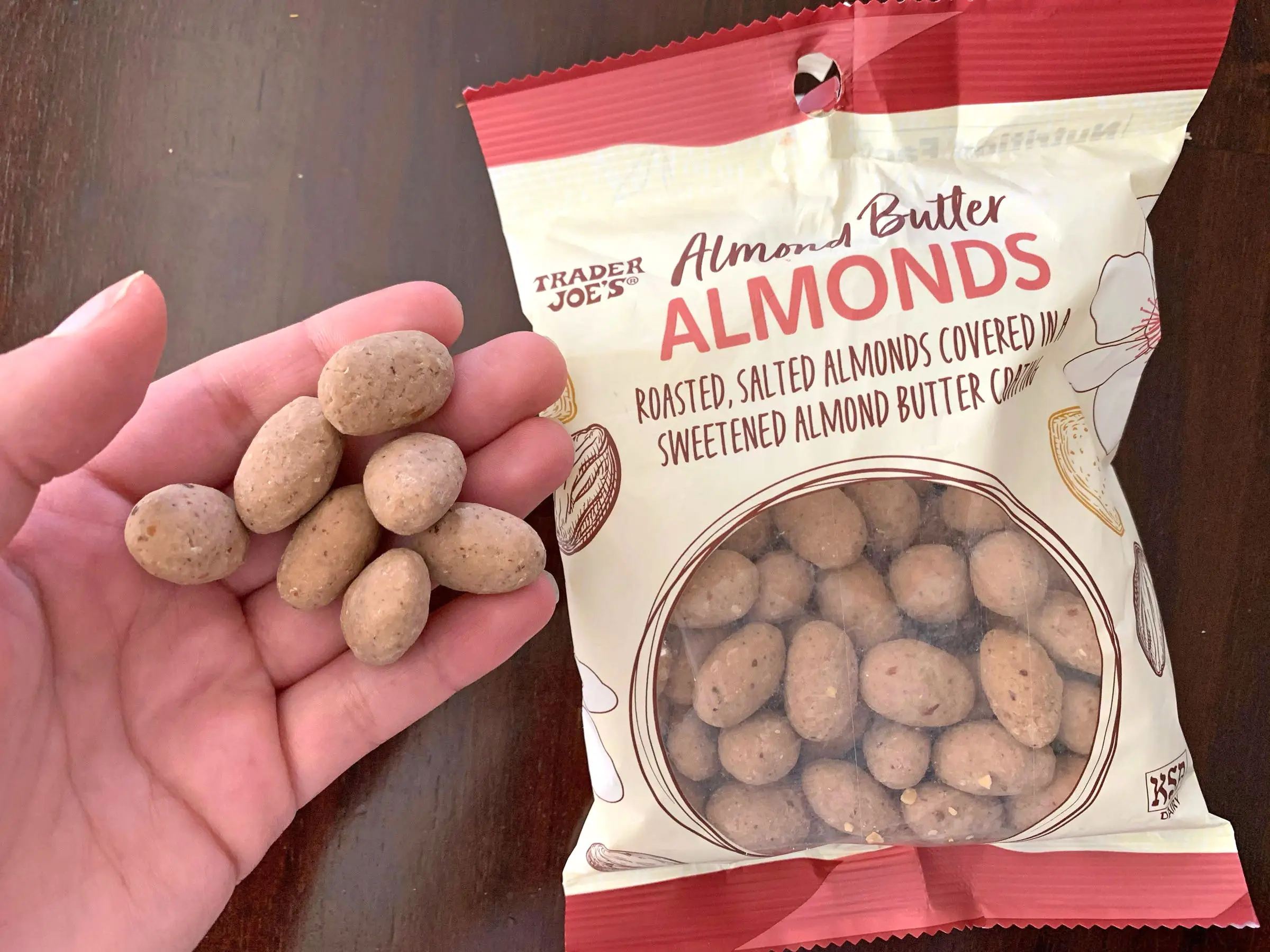 A hand holding coated almonds next to the bag the product came in.