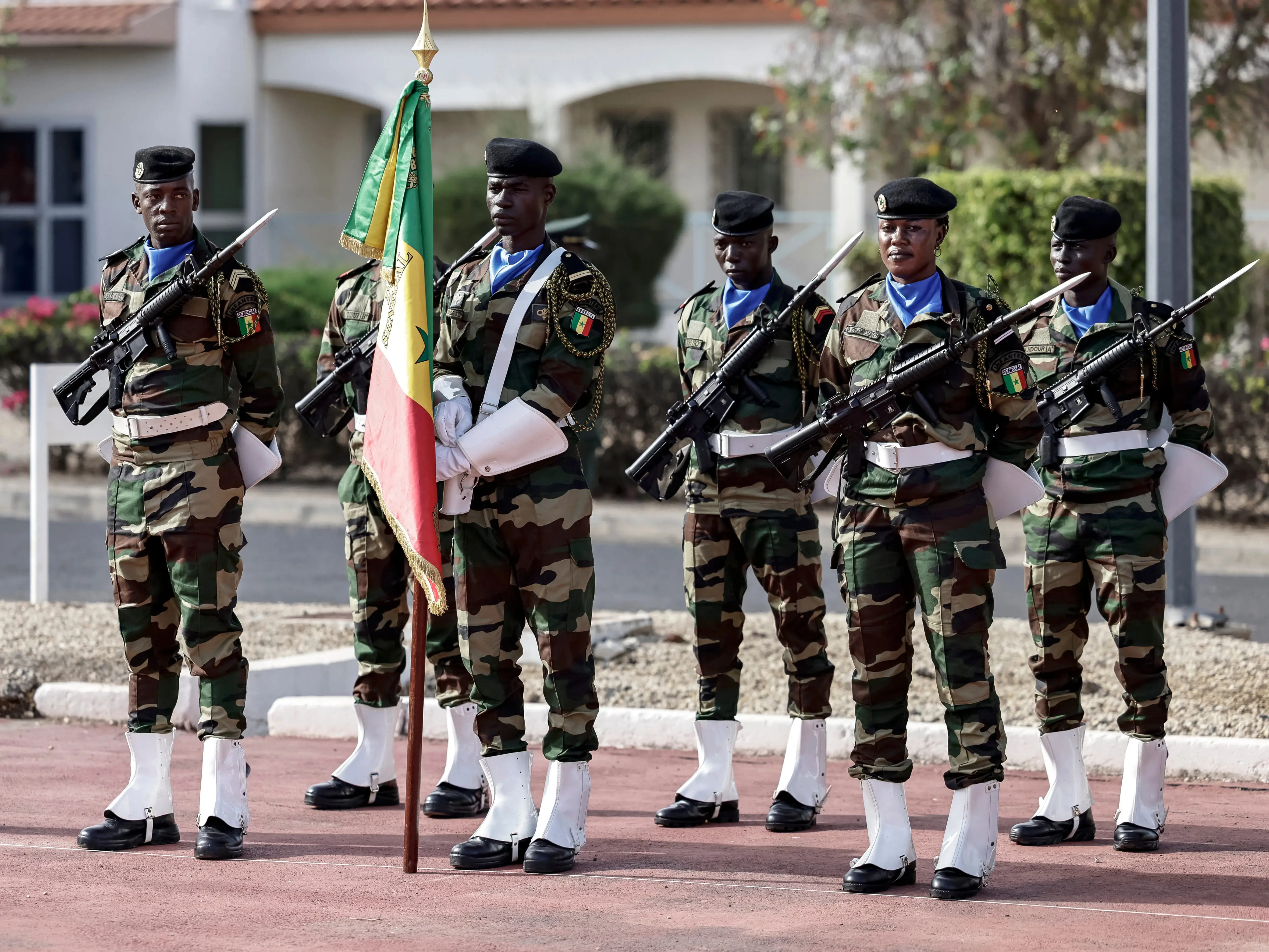 Members of the Senegalese army hold rifles behind a Senegal flag.