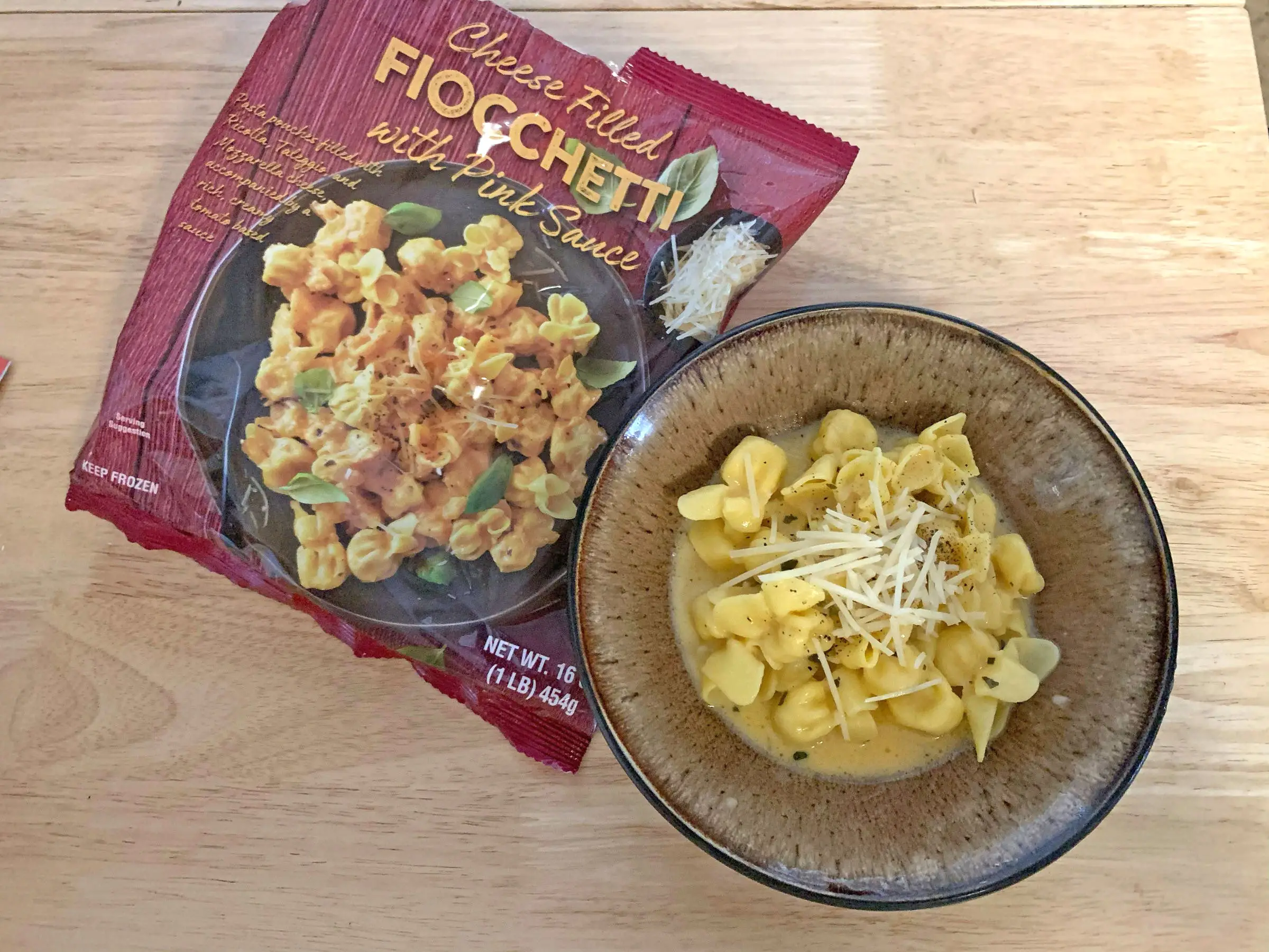 A bowl of Trader Joe's fiocchetti in a cream sauce next to the bag the product came in.