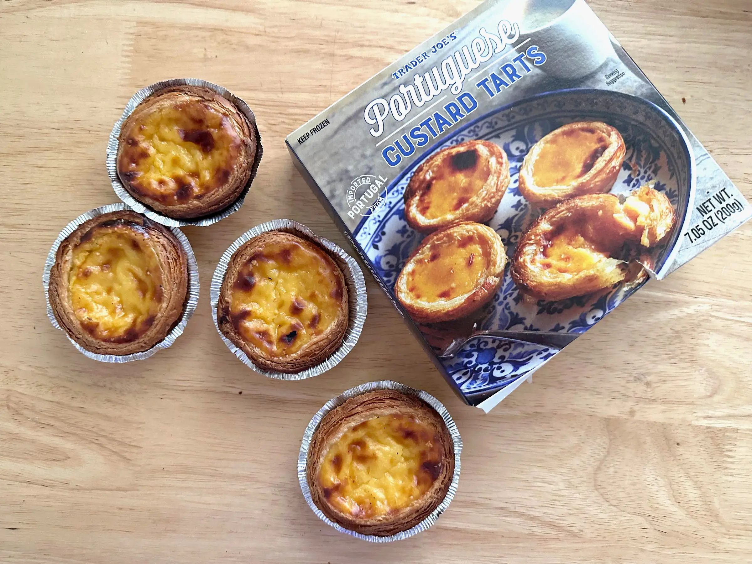 Four Trader Joe's Portuguese custard tarts next to the box they came in.