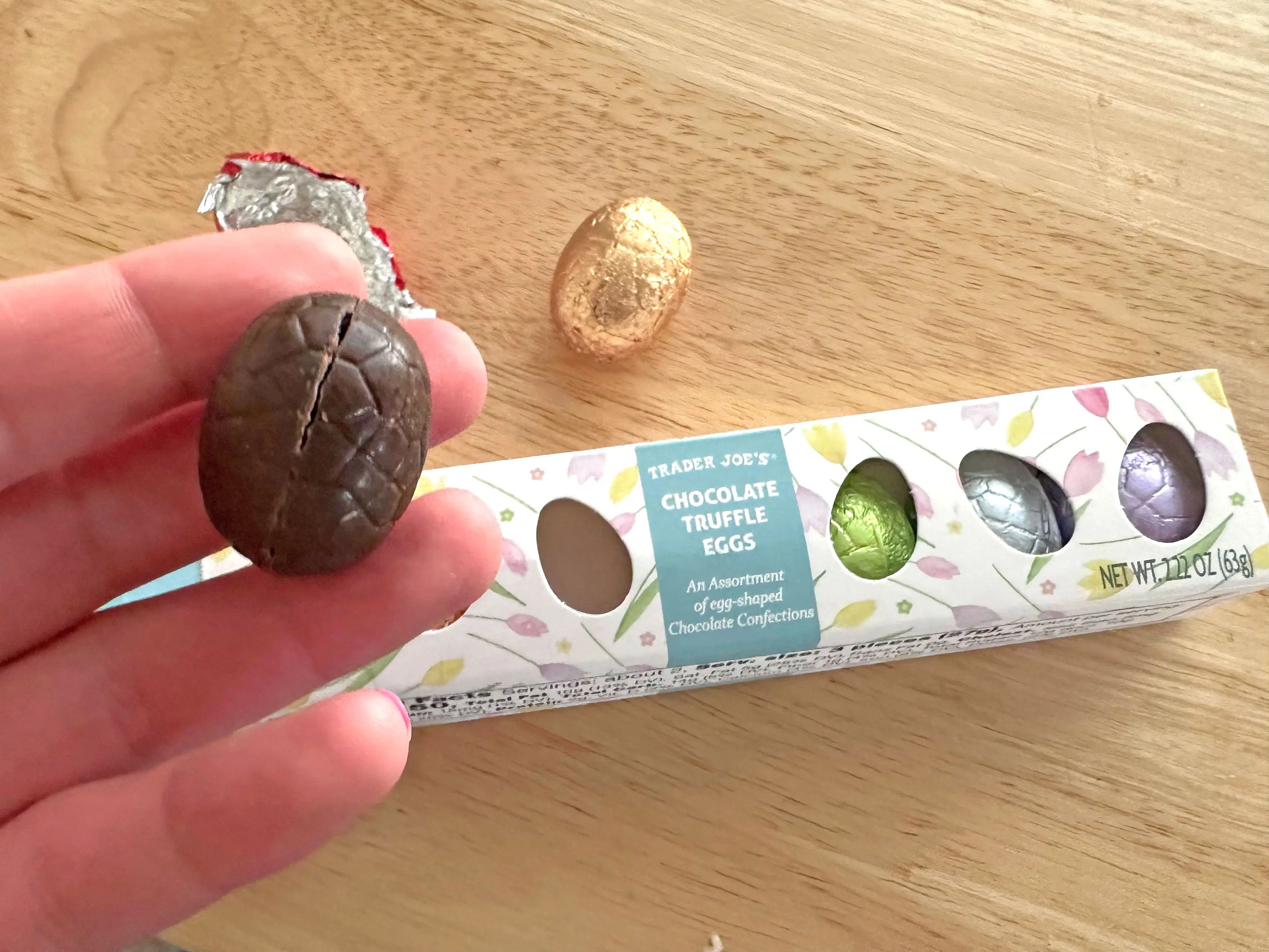 A hand holding an unwrapped chocolate egg over a box of Trader Joe's chocolate truffle eggs.