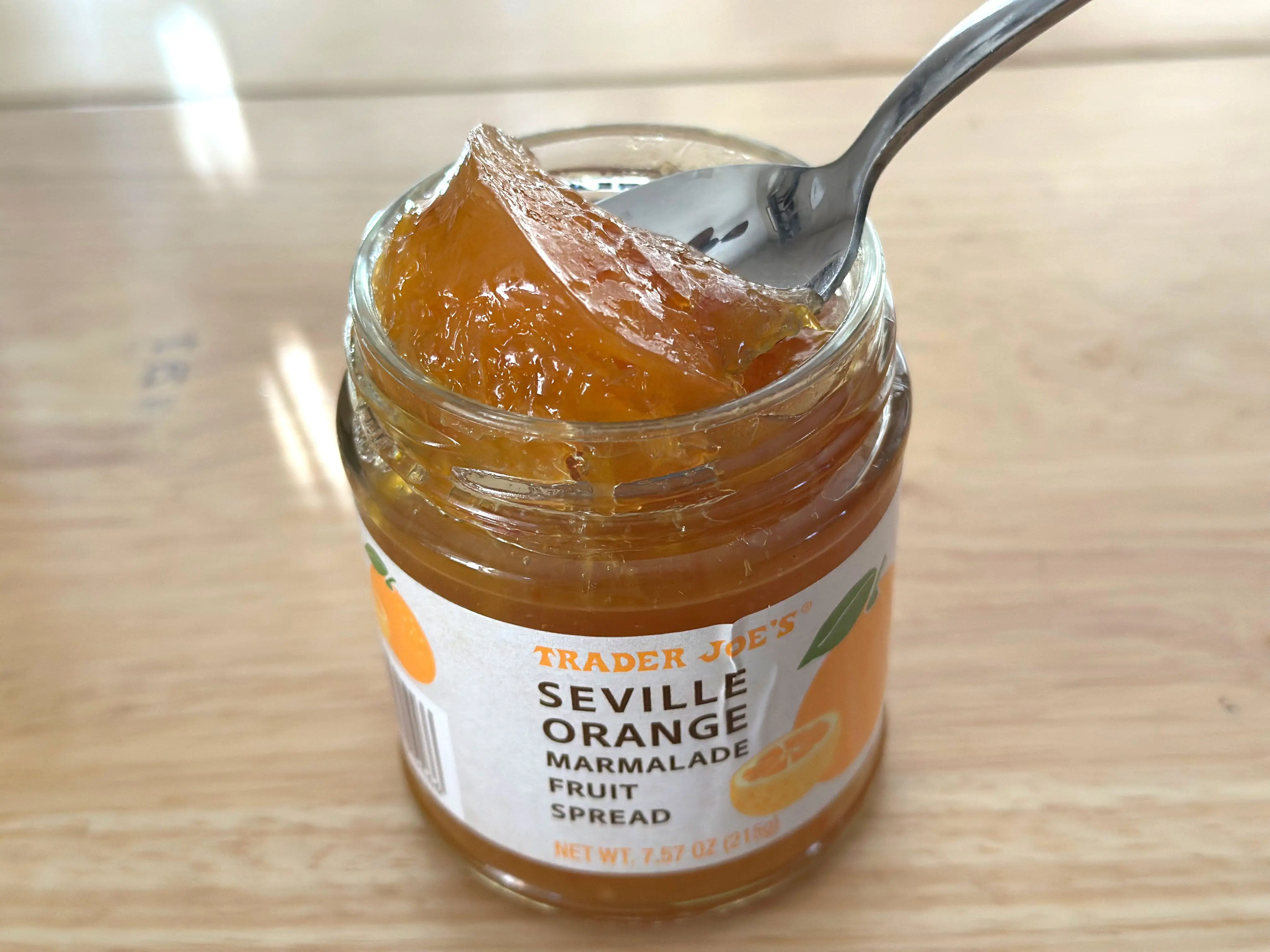 A spoon scooping orange marmalade out of a jar.