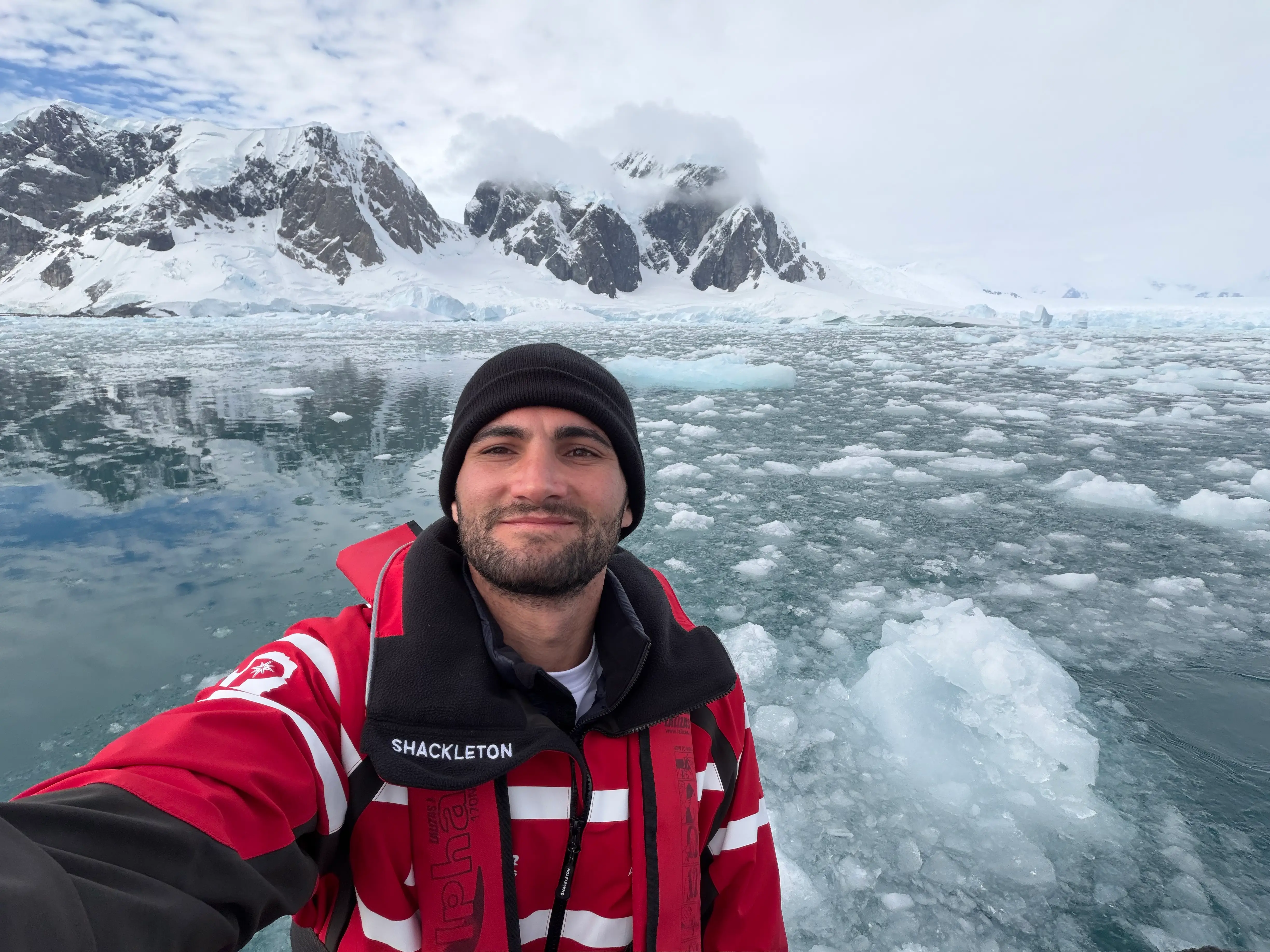 Man in a red jacket with ice behind him in Antarctica.
