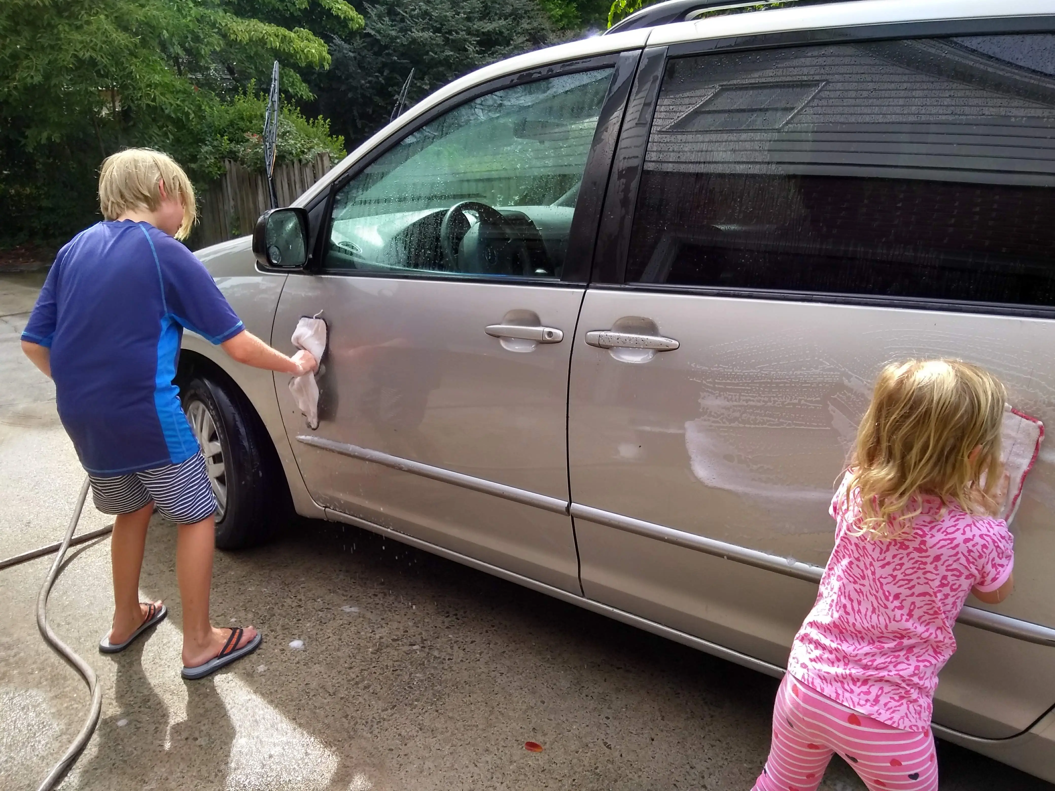 Two kids work together to clean the family car.