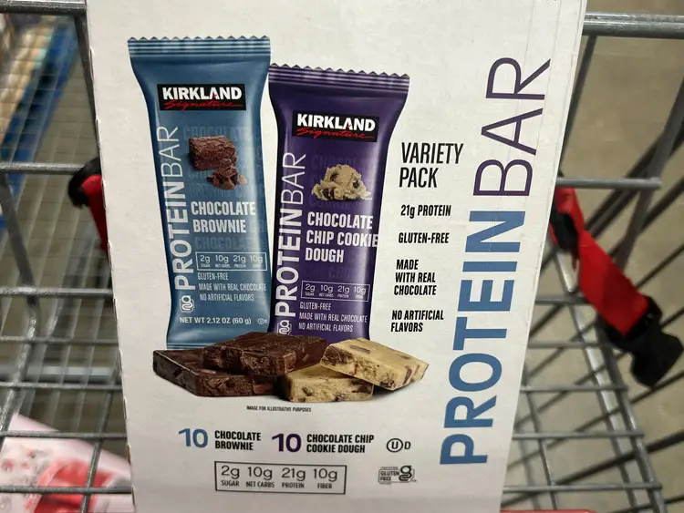 A box of Kirkland Signature protein bars in a Costco shopping cart.