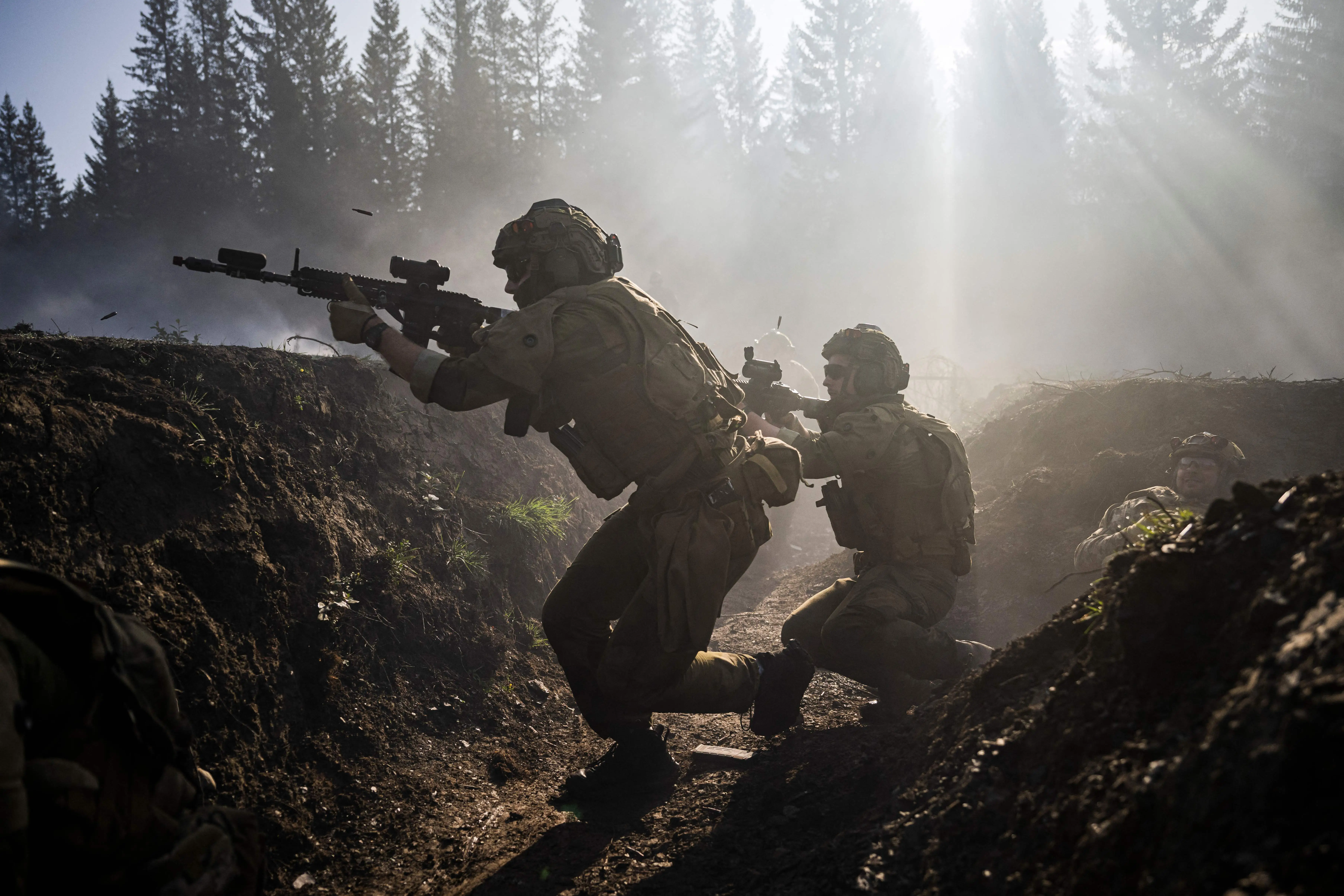 Two figures wearing camouflage hold firearms in the air and run inside a trench with mist and trees behind them