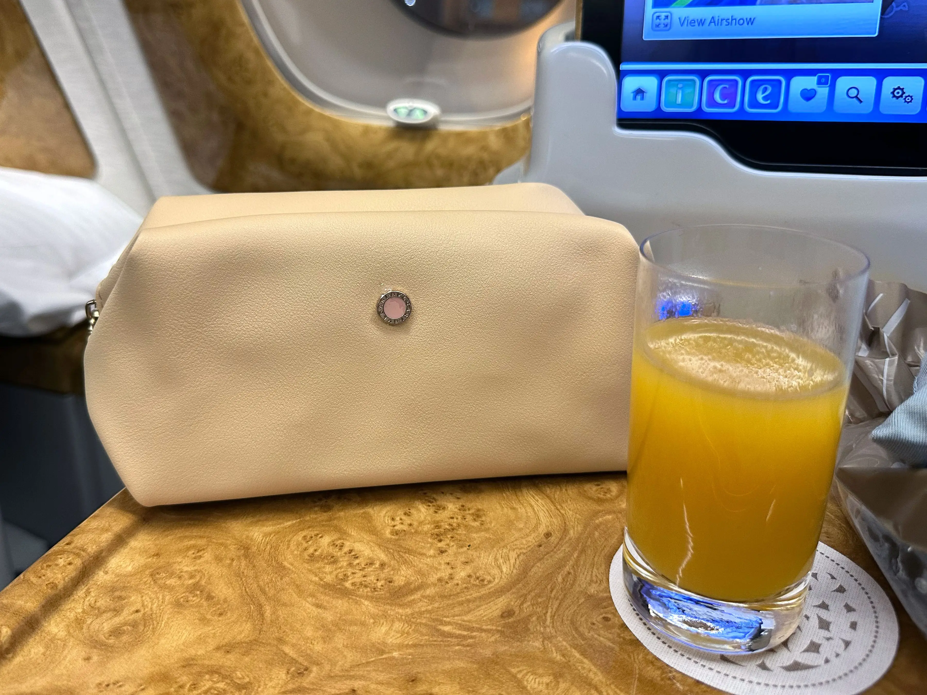 A glass of juice and a makeup bag on a plane tray.