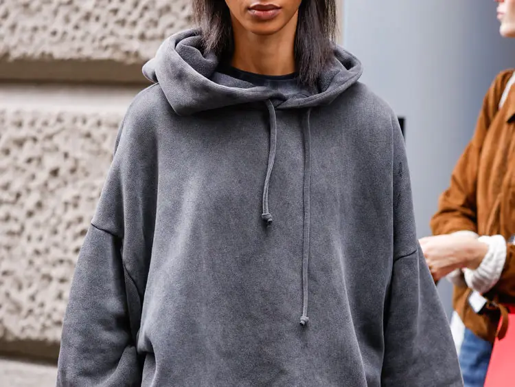 A woman wearing an oversize gray hoodie.