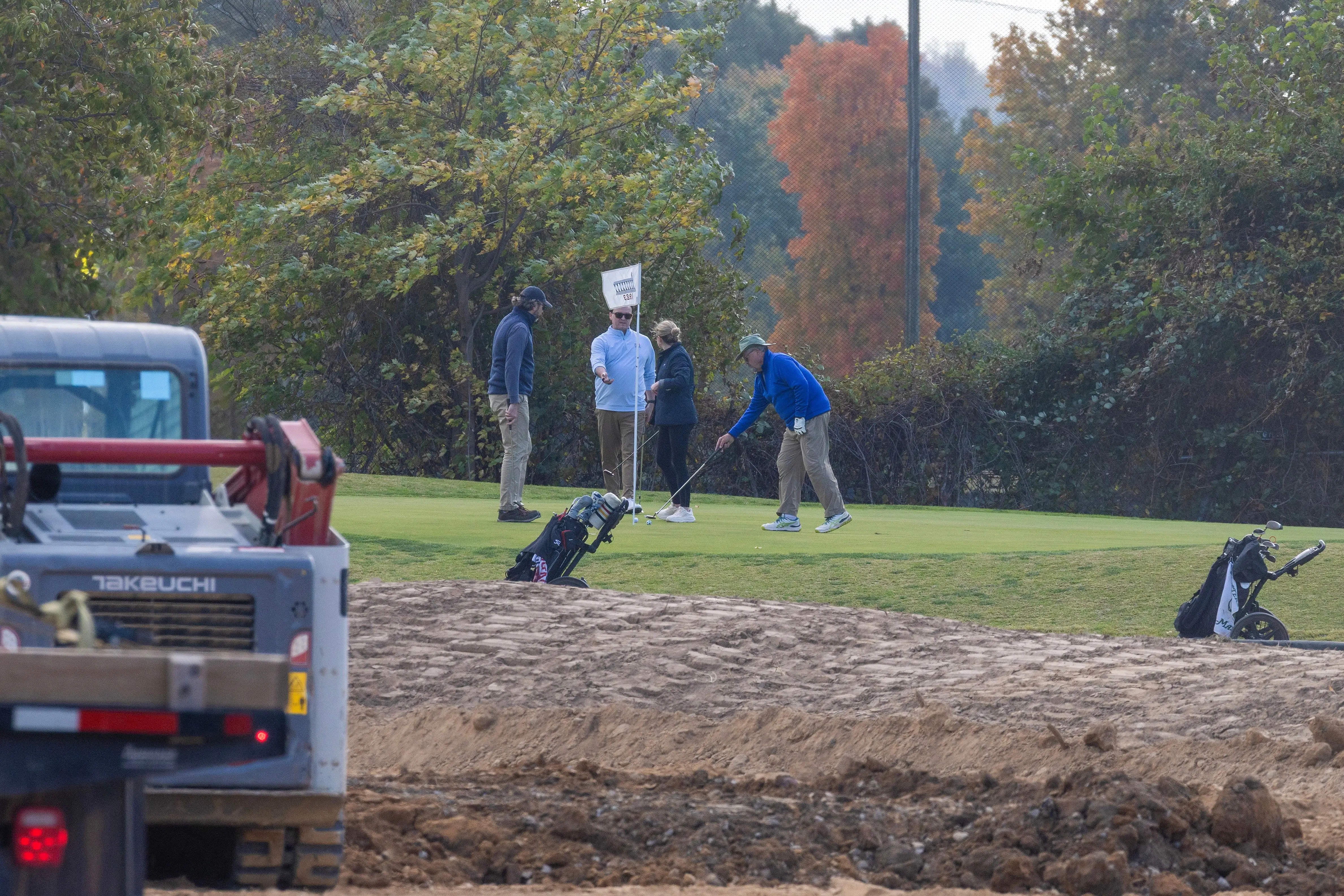 Golfers play hole six as trucks unloads debris and soil from the demolition of the White House's East Wing at East Potomac Golf Course on October 24, 2025 in Washington, DC.