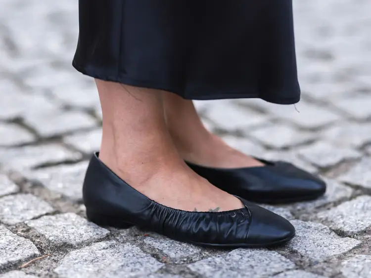 A woman wearing a pair of black flat shoes.