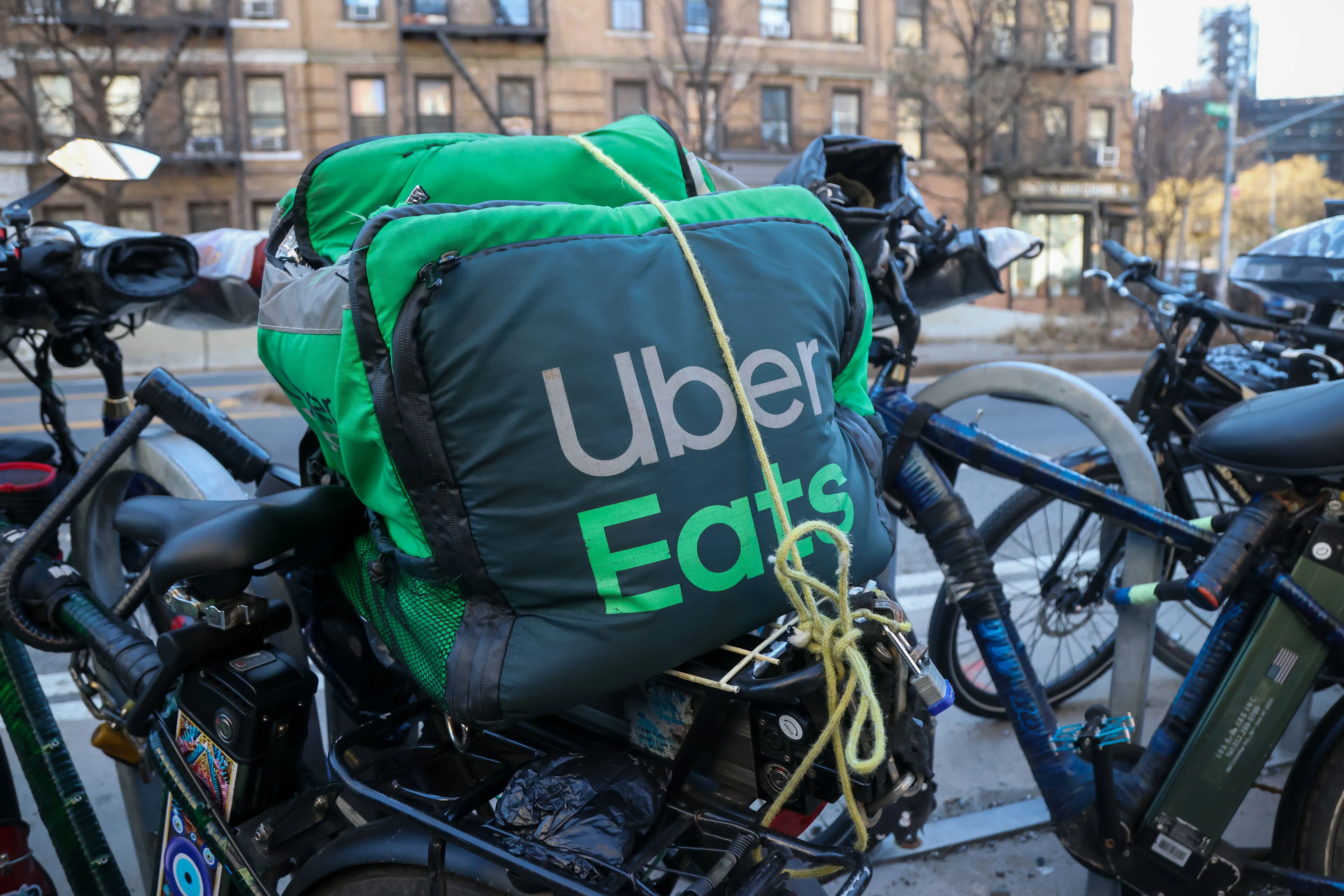 A black-and-green Uber Eats insulated bag sits tied onto the back of a bicycle on a sidewalk.