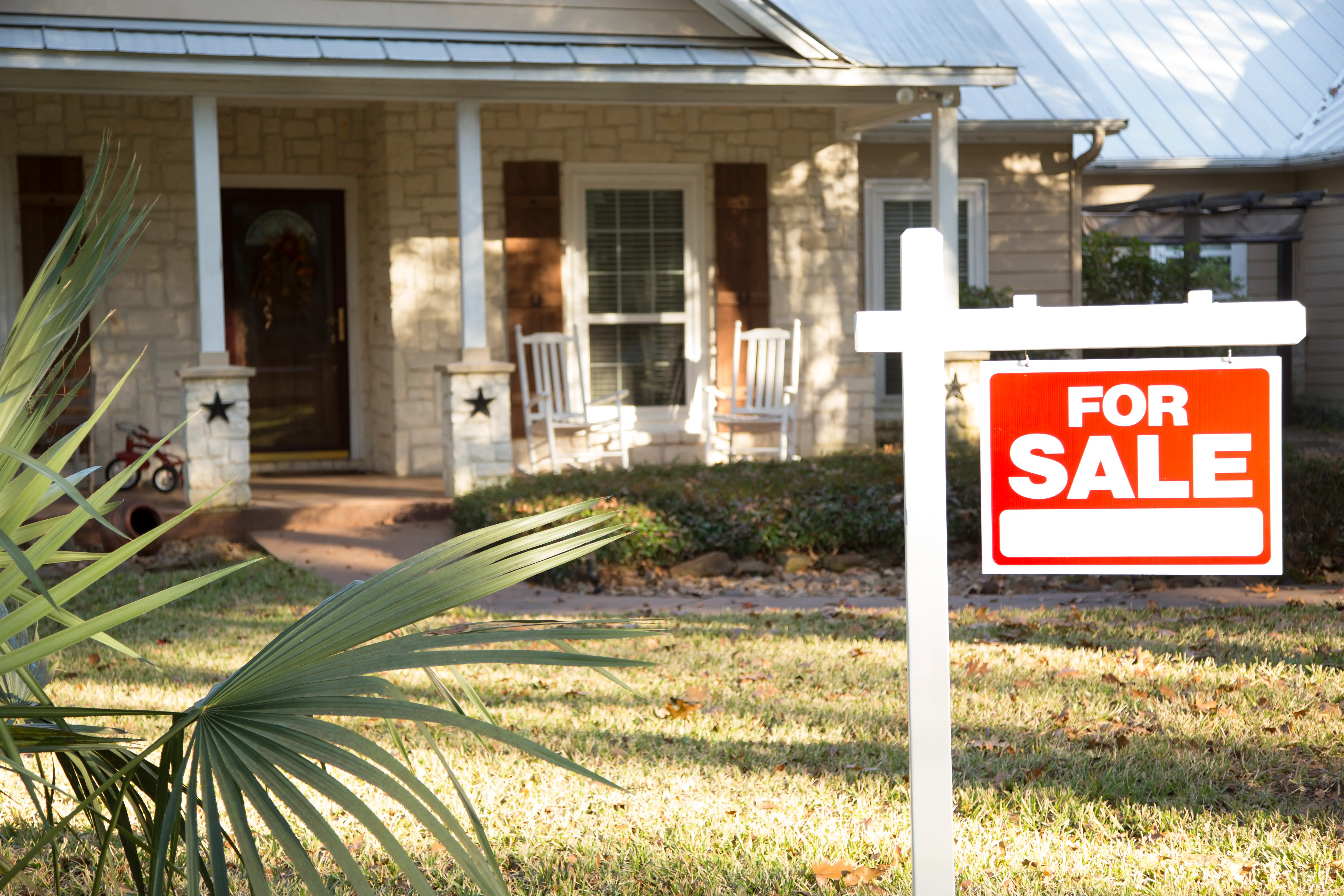 A rustic, ranch-style home with a for-sale sign in the front yard.