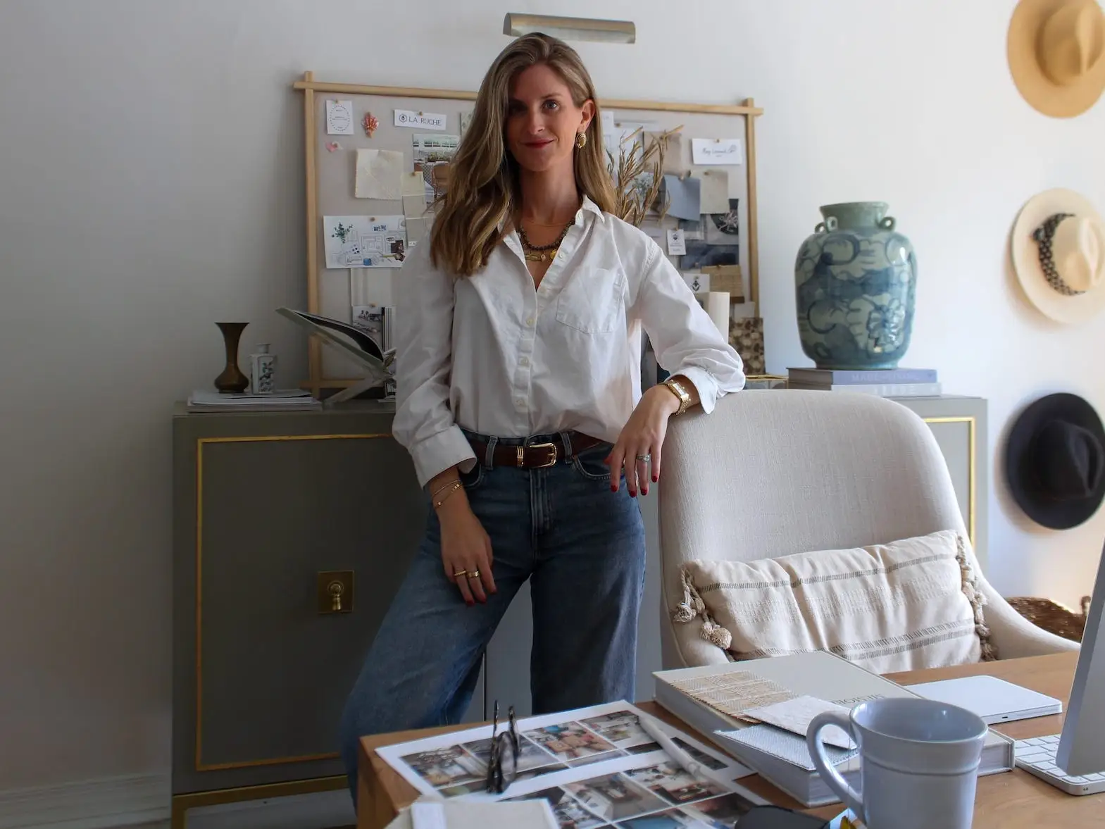 A woman stands in her office in front of a bulletin board with her arm leaning on a chair.