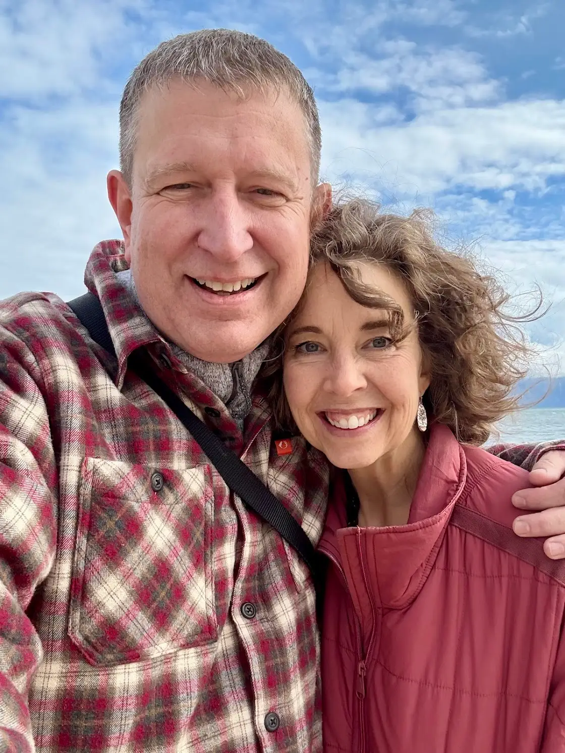 Man and woman wearing red and posing with water in the background.
