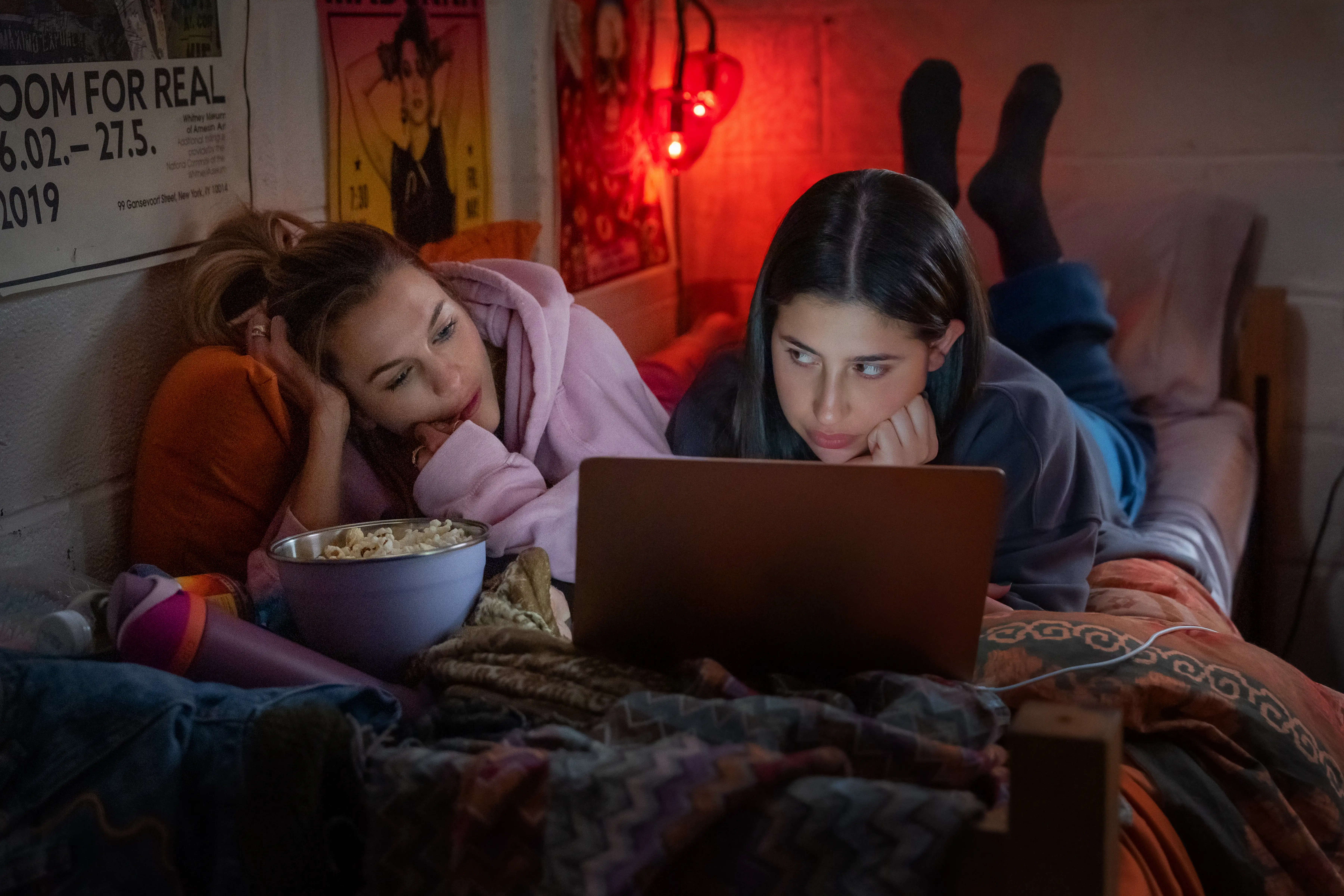 Chloe East and Sadie Sandler on a bed looking at a laptop in Roommates