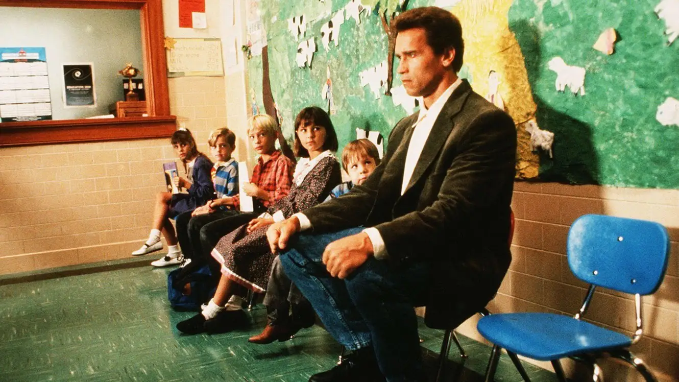 Arnold Schwarzenegger sitting next to small kids in an office in Kindergarten Cop