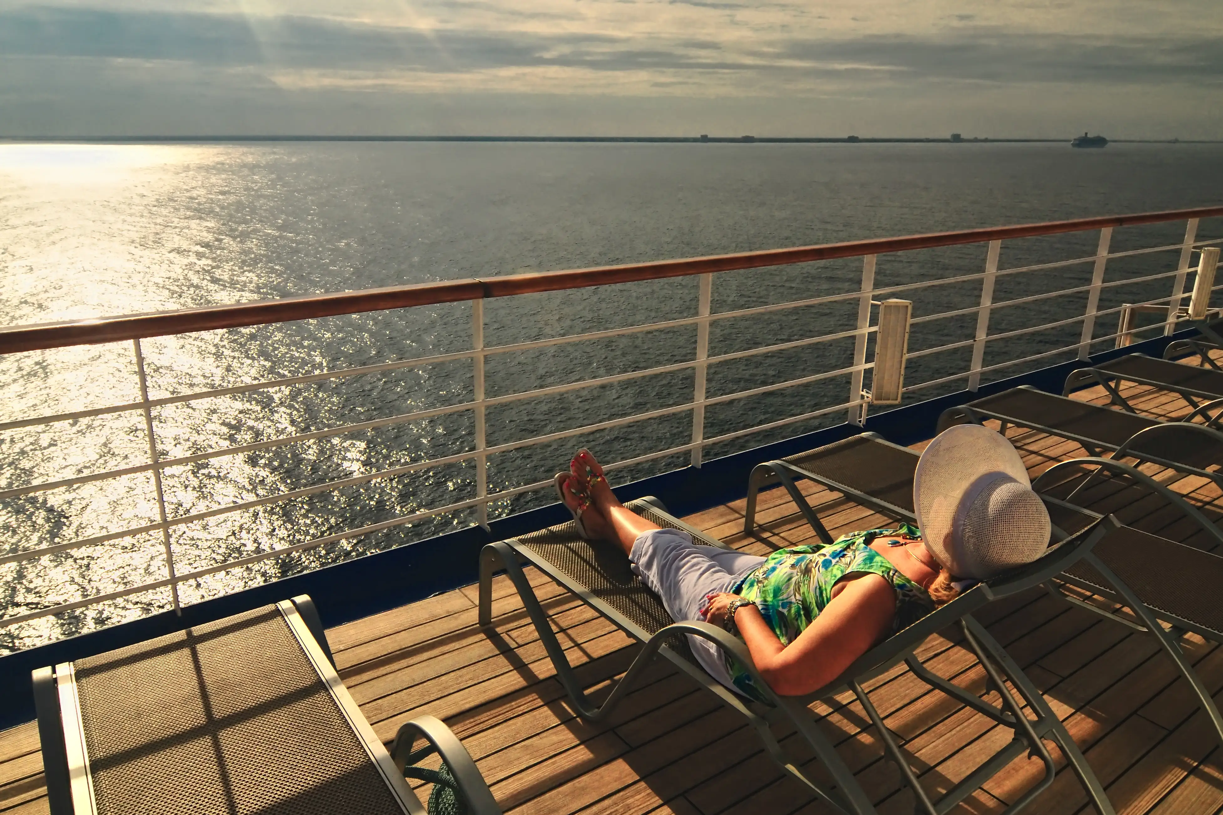 woman in a sunbonnet relaxes on the top deck of a cruise ship during her vacation at sea