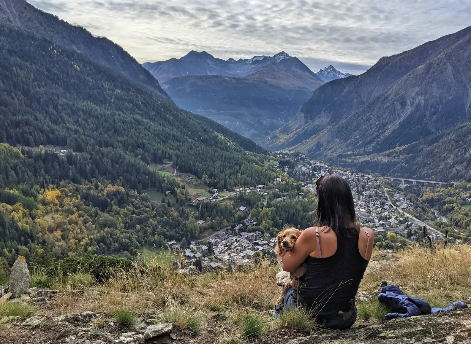 The writer and her dog sitting on a rock in the mountains, overlooking a town.