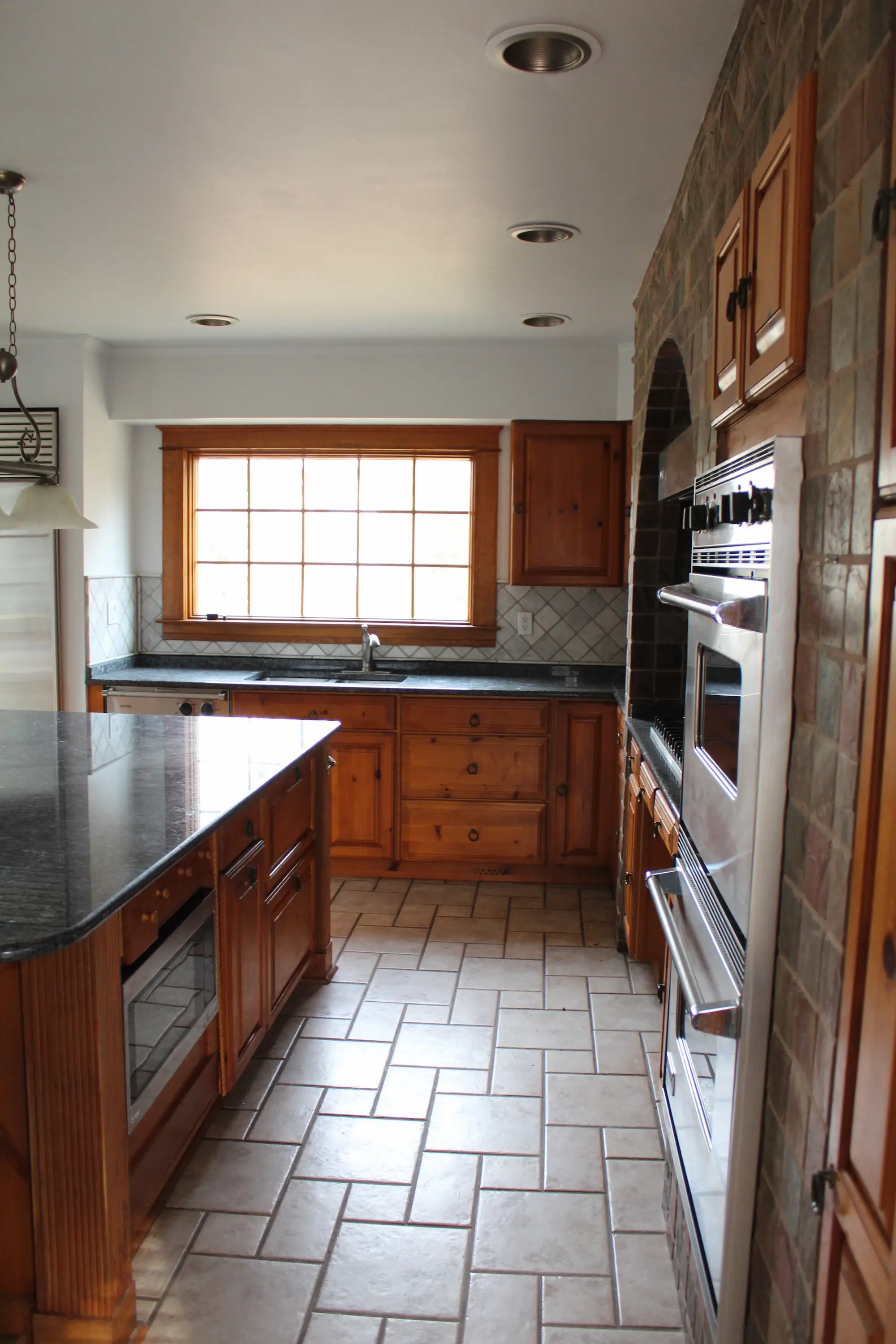A kitchen with stone floors and wooden cabinetry.