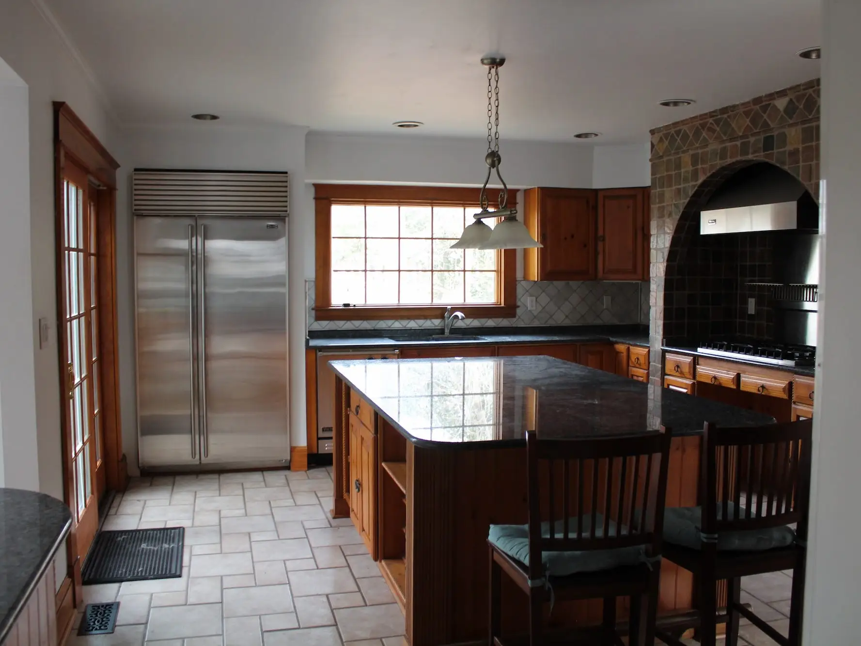 A kitchen with a large island, wood cabinetry, and dark countertops.