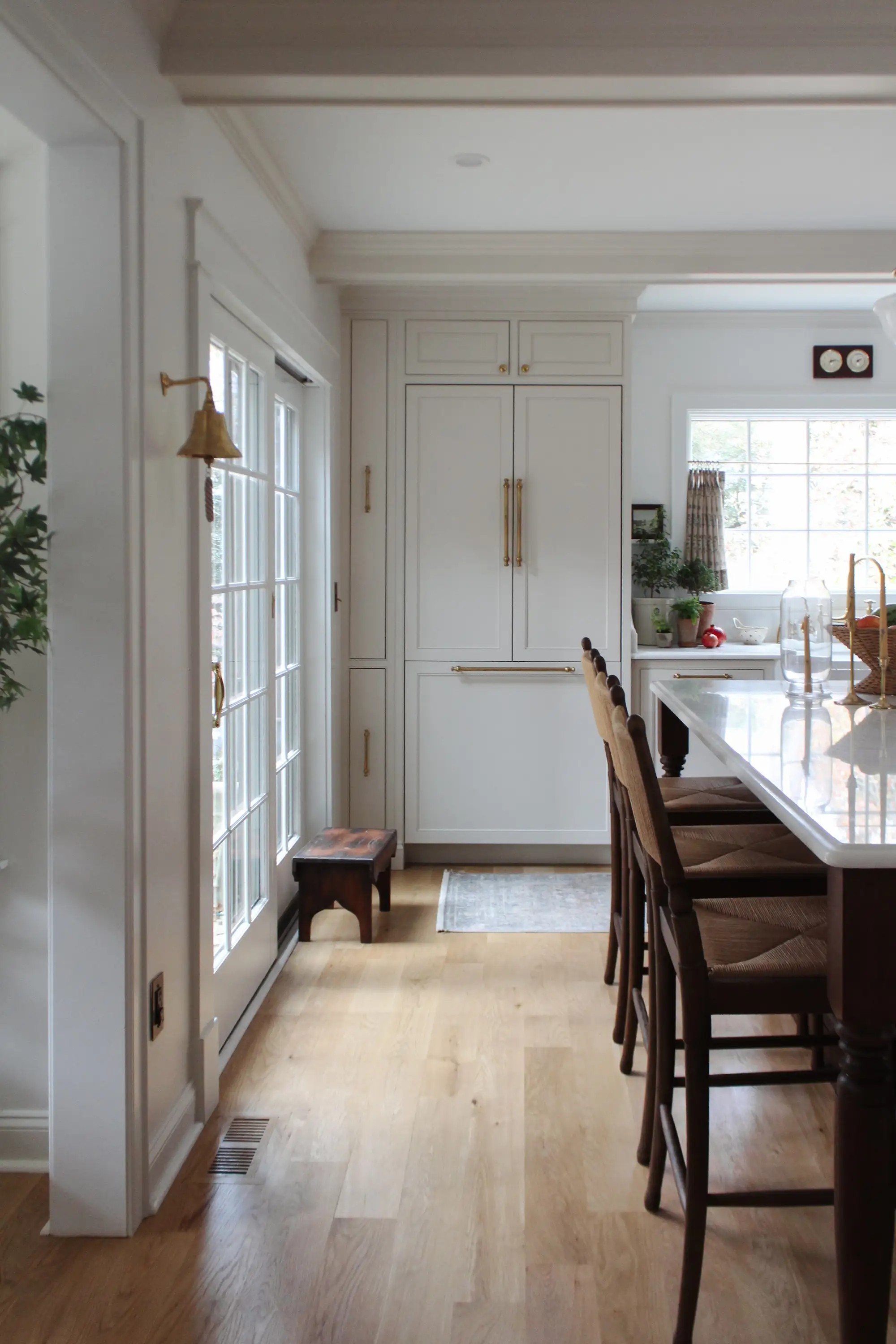 A kitchen with white cabinetry and a white refrigerator with gold trim. A large door on the left leads outside.