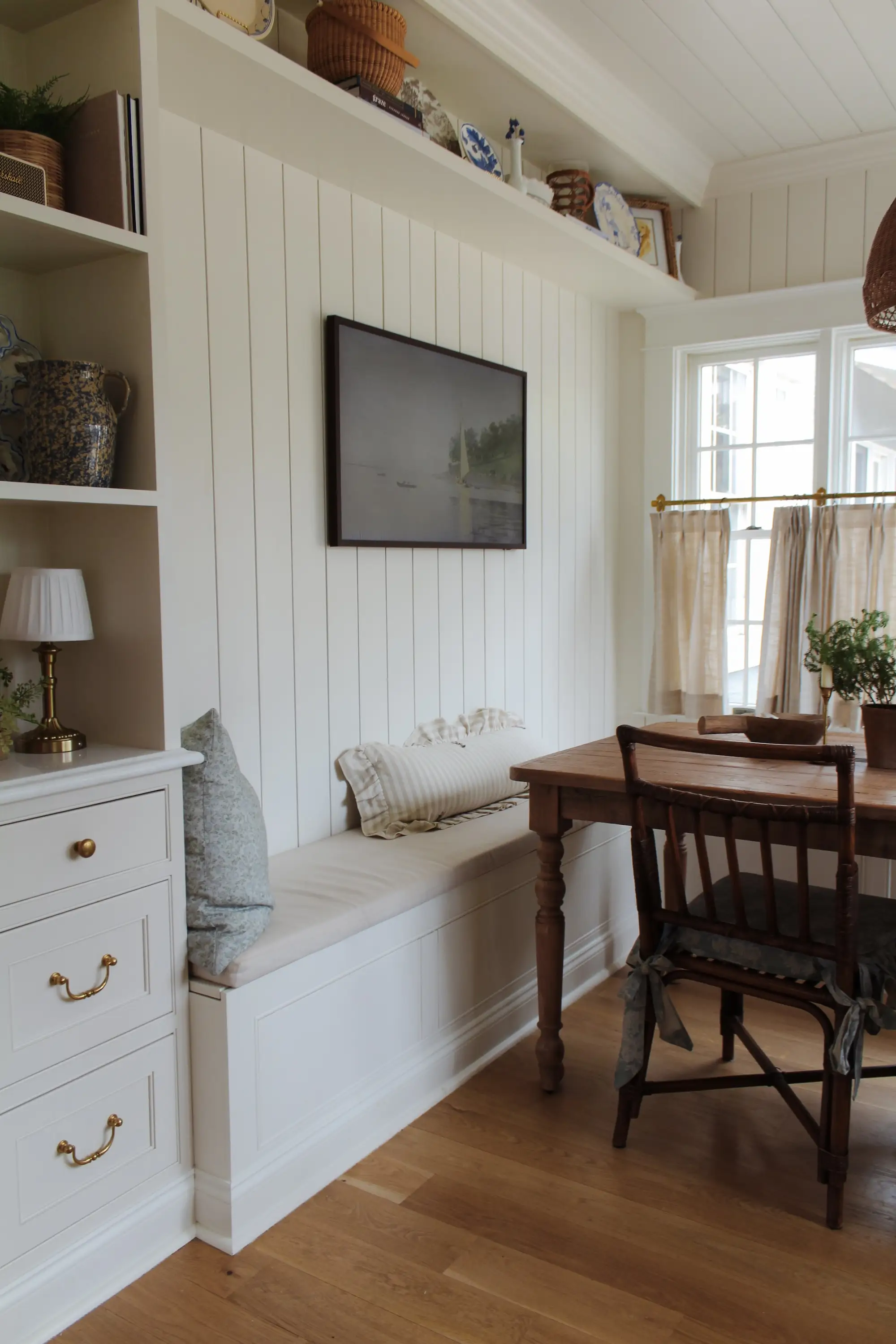 A kitchen with a bench seating area with open shelving and shiplap walls.