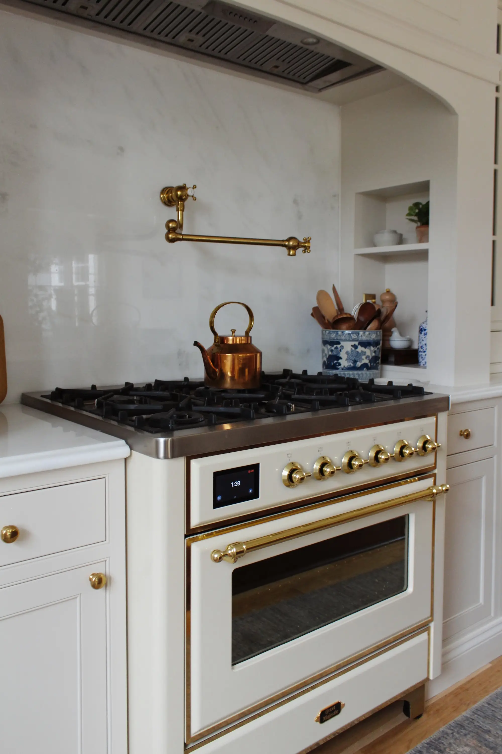 A stove and white oven surrounded by marble backsplash and cream cabinetry.