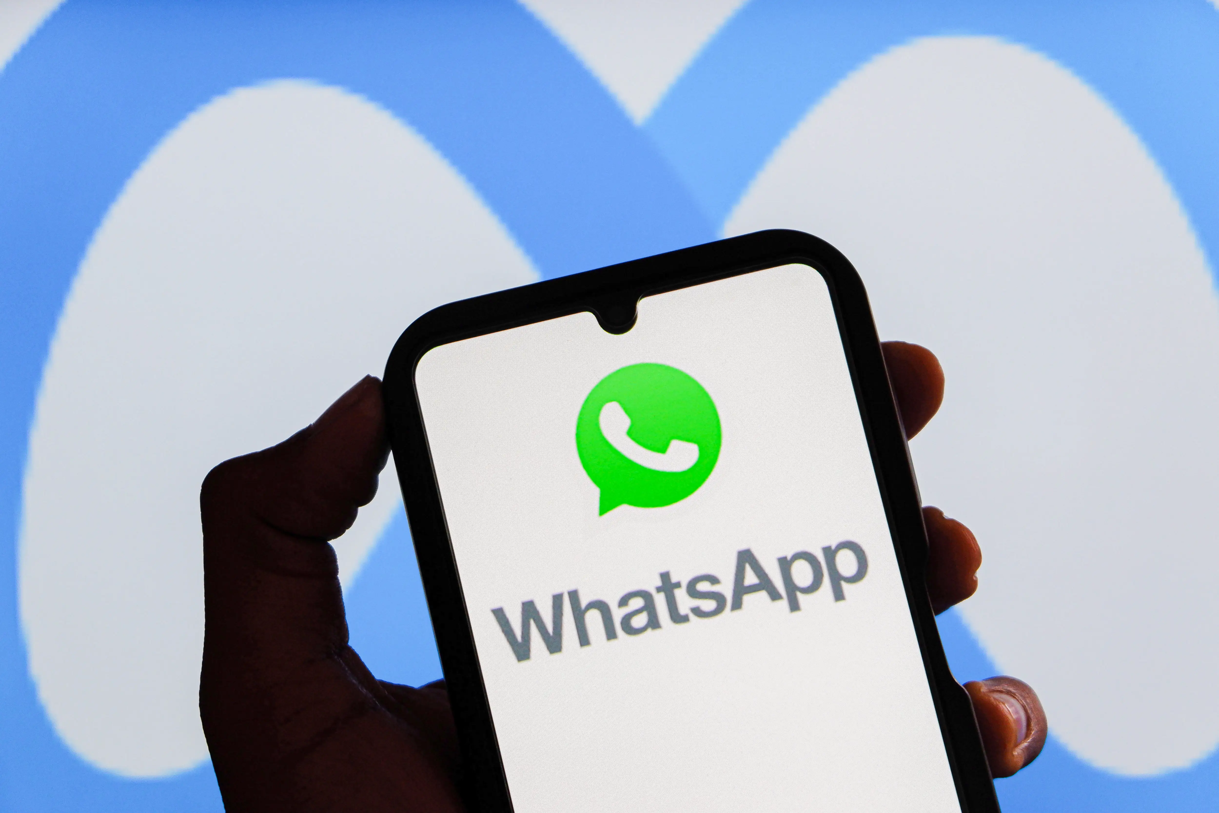A man holding a phone with the WhatsApp logo on the screen.