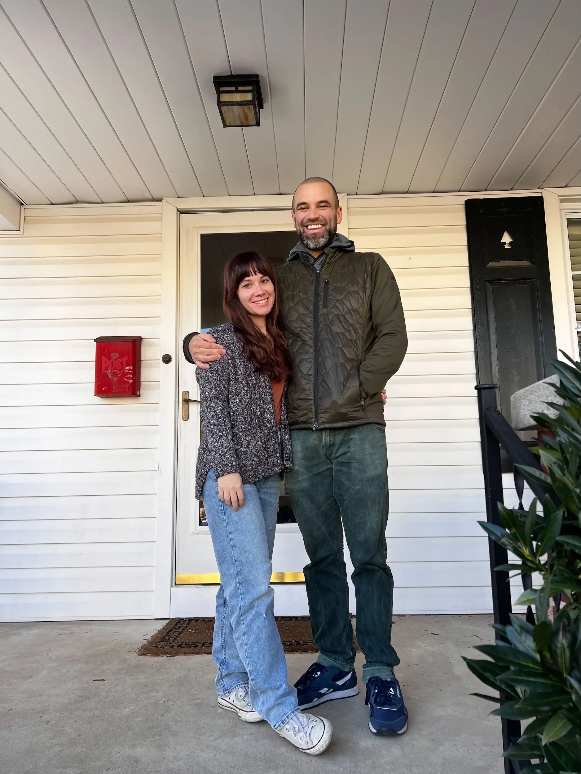 A man and a woman posing for a picture in front of a house.