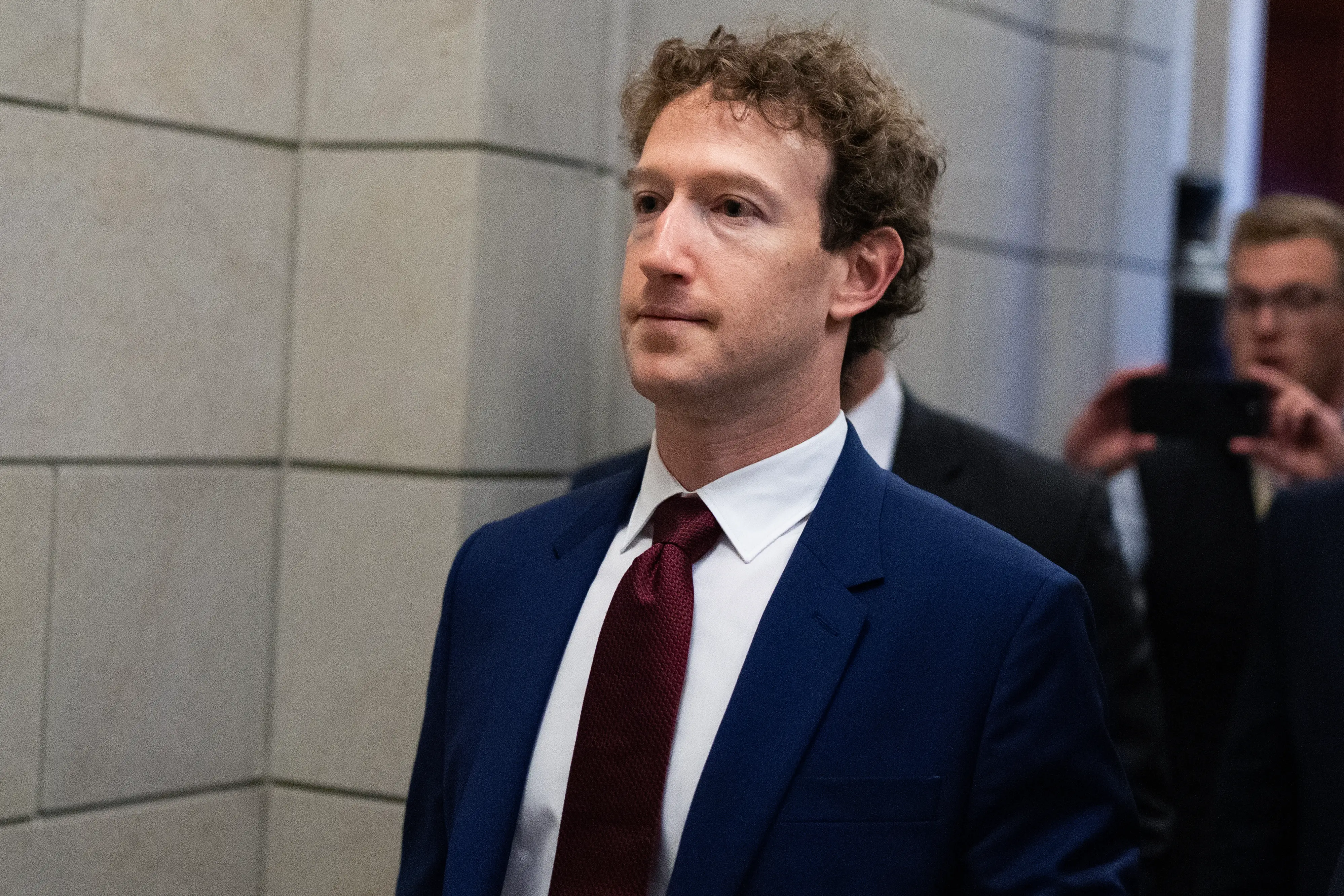 Mark Zuckerberg wears a navy suit and burgundy tie walking at the US Capitol.