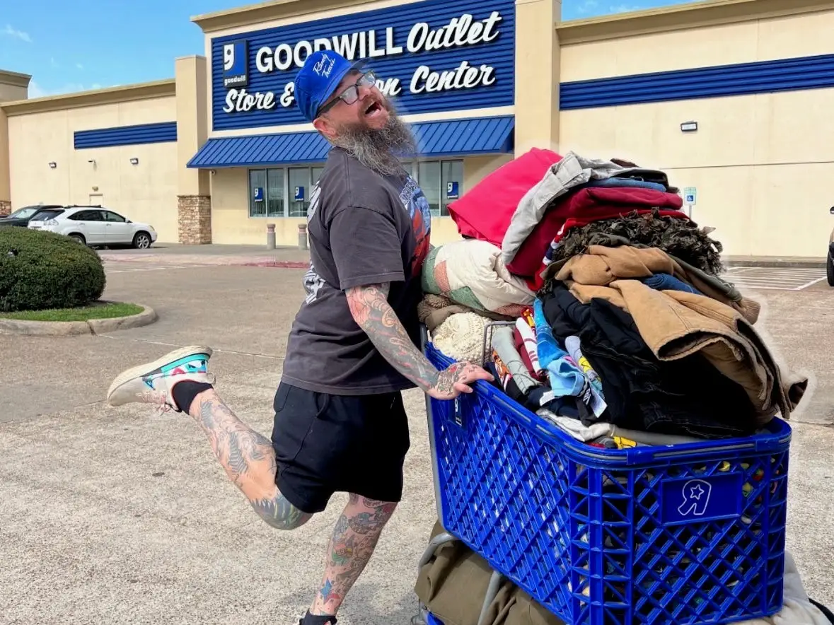 A man standing outside of Goodwill posing with a cart.