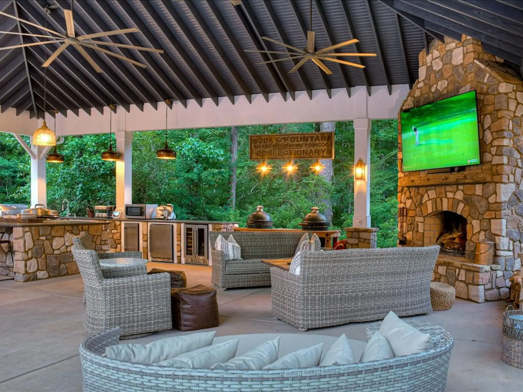 An open-air, covered patio with a TV screen, outdoor kitchen, and fans on the ceiling.