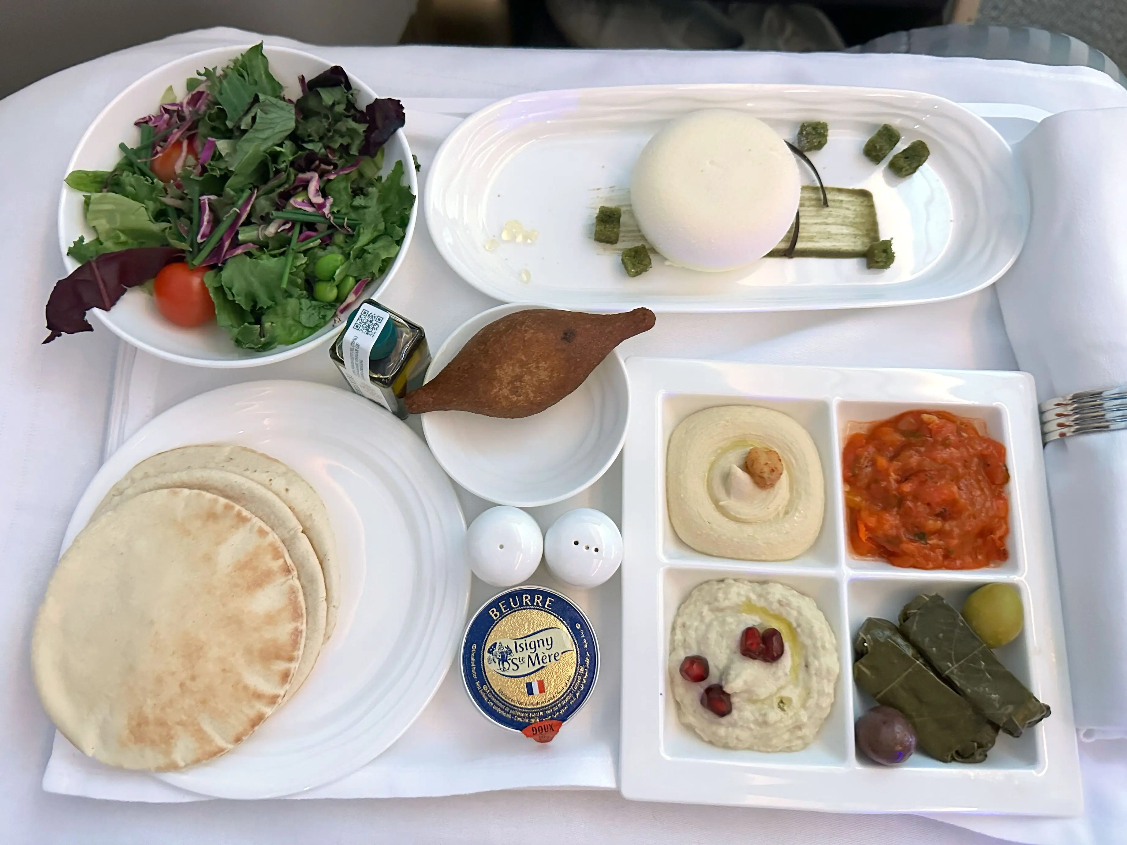 A salad, pita, cheese, and multiple spreads on a white tablecloth.