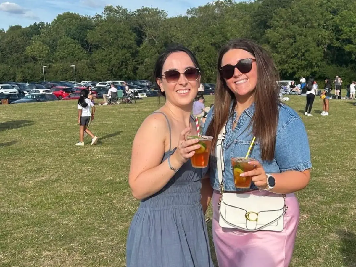 The writer and a friend holding drinks and standing in a field in Milton Keynes.