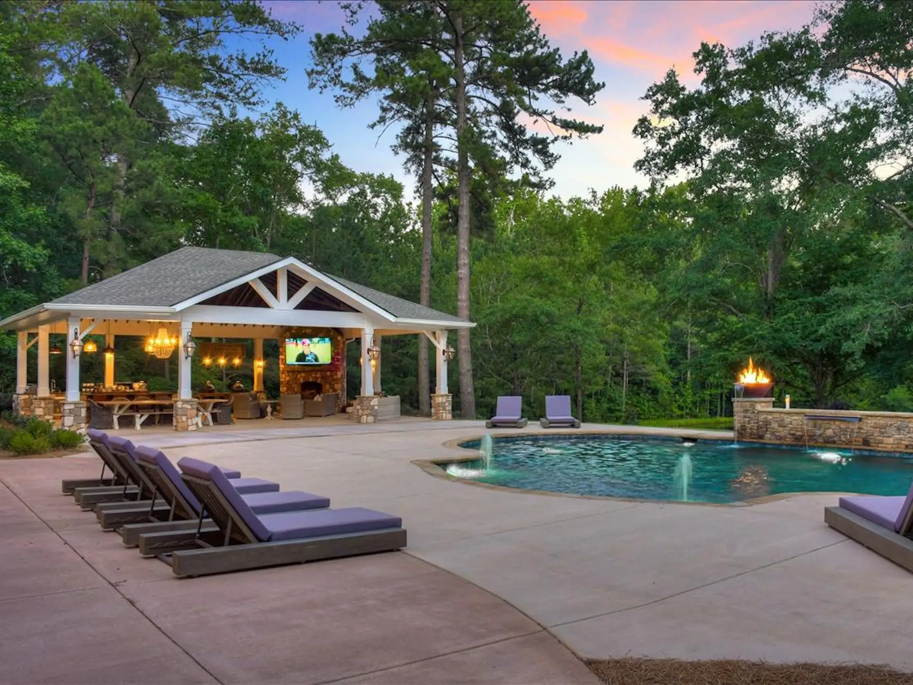 A pool with a large covered patio sitting nearby and greenery in the back.