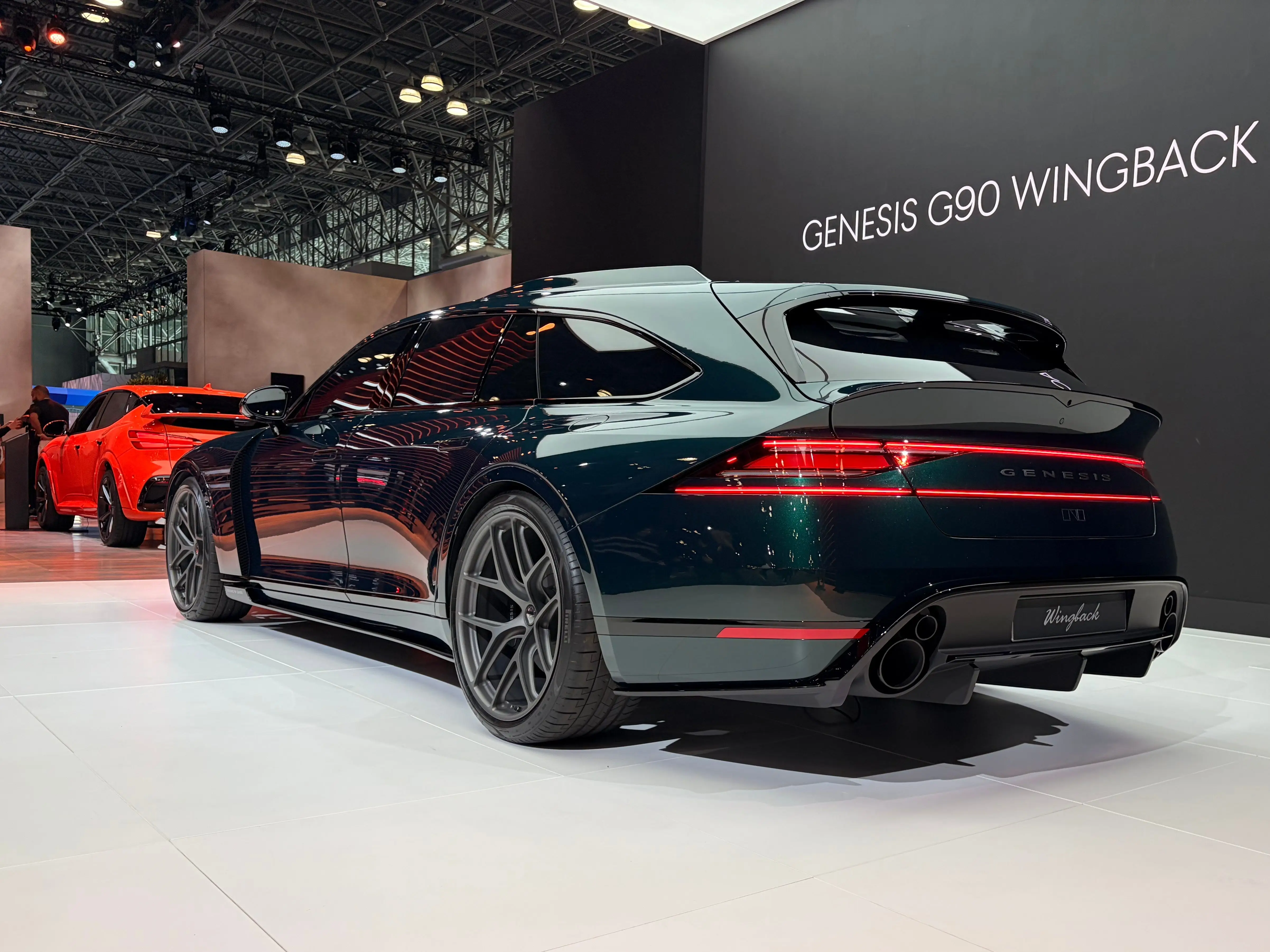 A dark green Genesis concept wagon is parked on a white tile floor at the New York International Auto Show. It has two light bars streaking across the back.