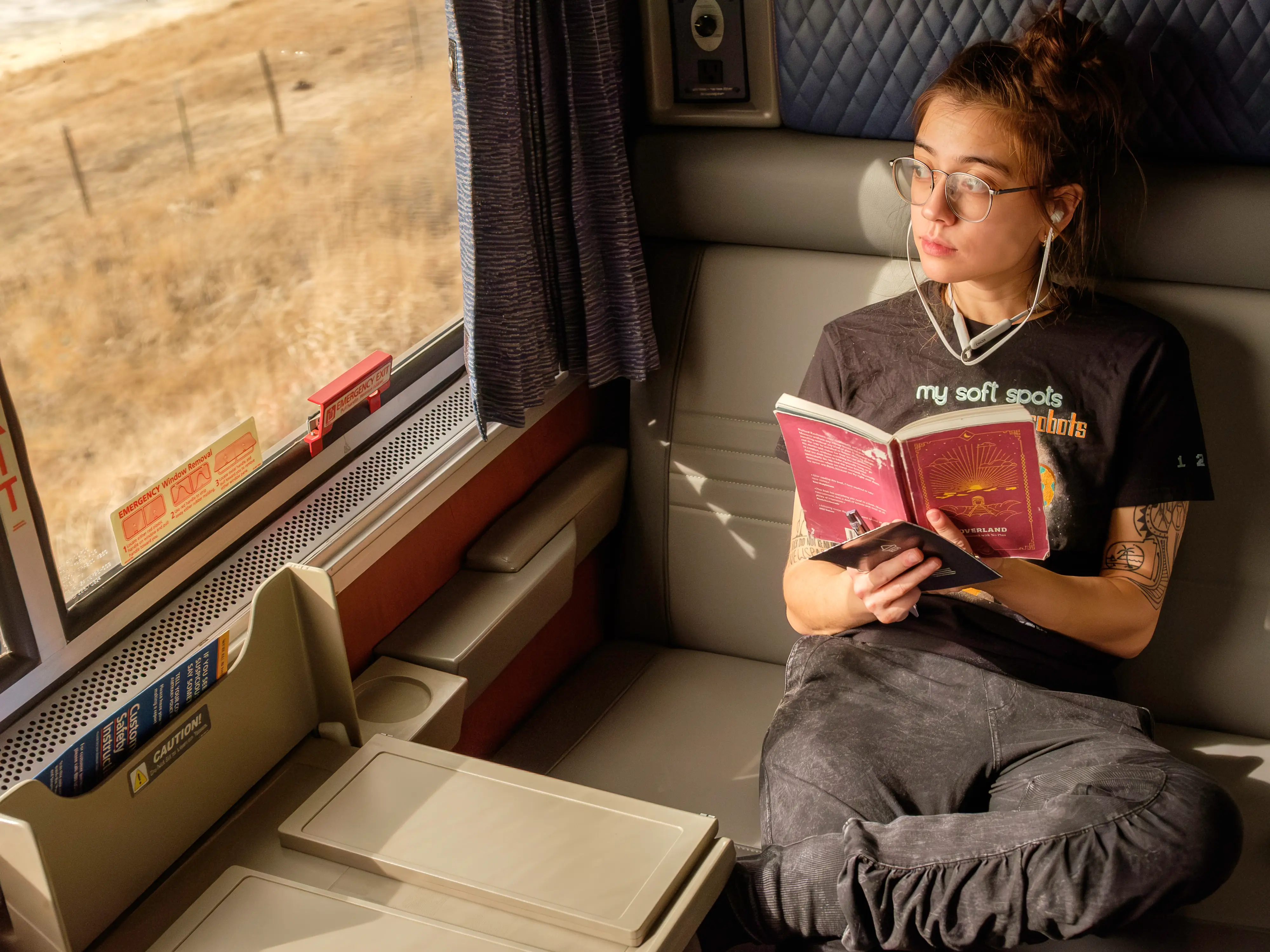 The author sits with a book in her hand looking out a train window to the left inside the Amtrak bedroom