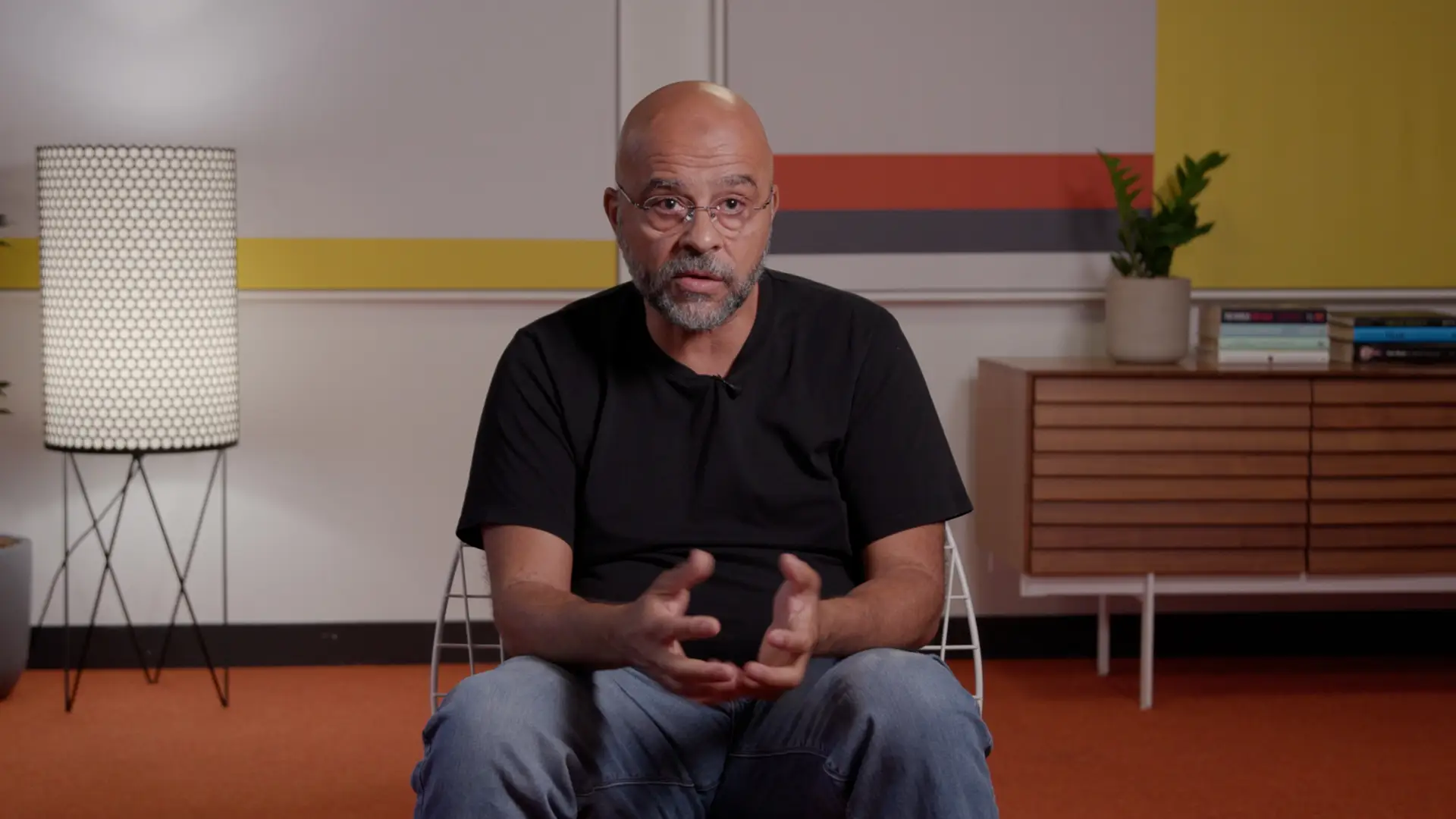 Mo Gawdat sitting in a chair in a black t-shirt and jeans.
