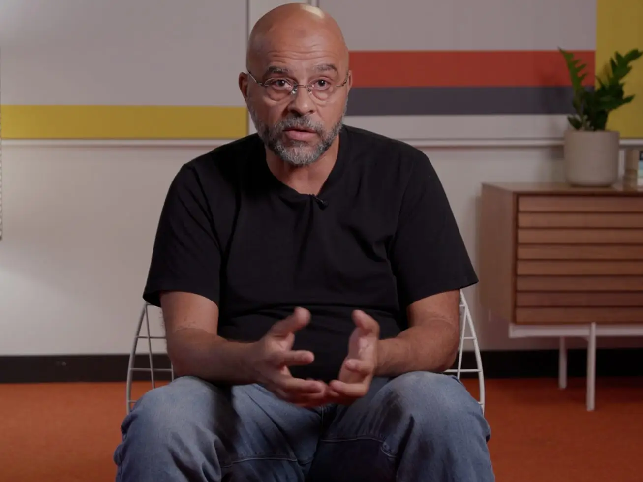Mo Gawdat sitting in a chair in a black t-shirt and jeans.