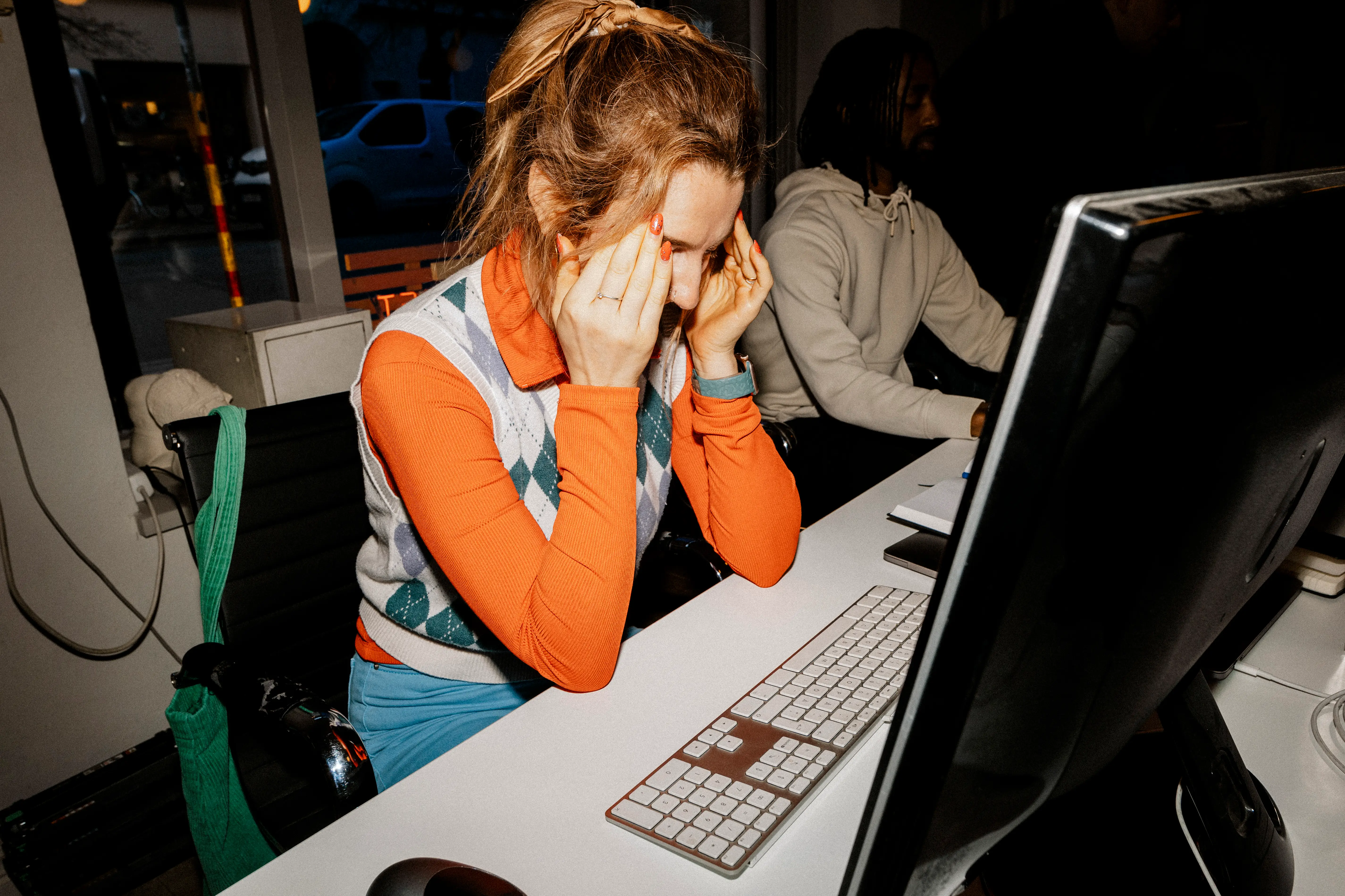 A woman is massaging her temples while sitting at a computer.