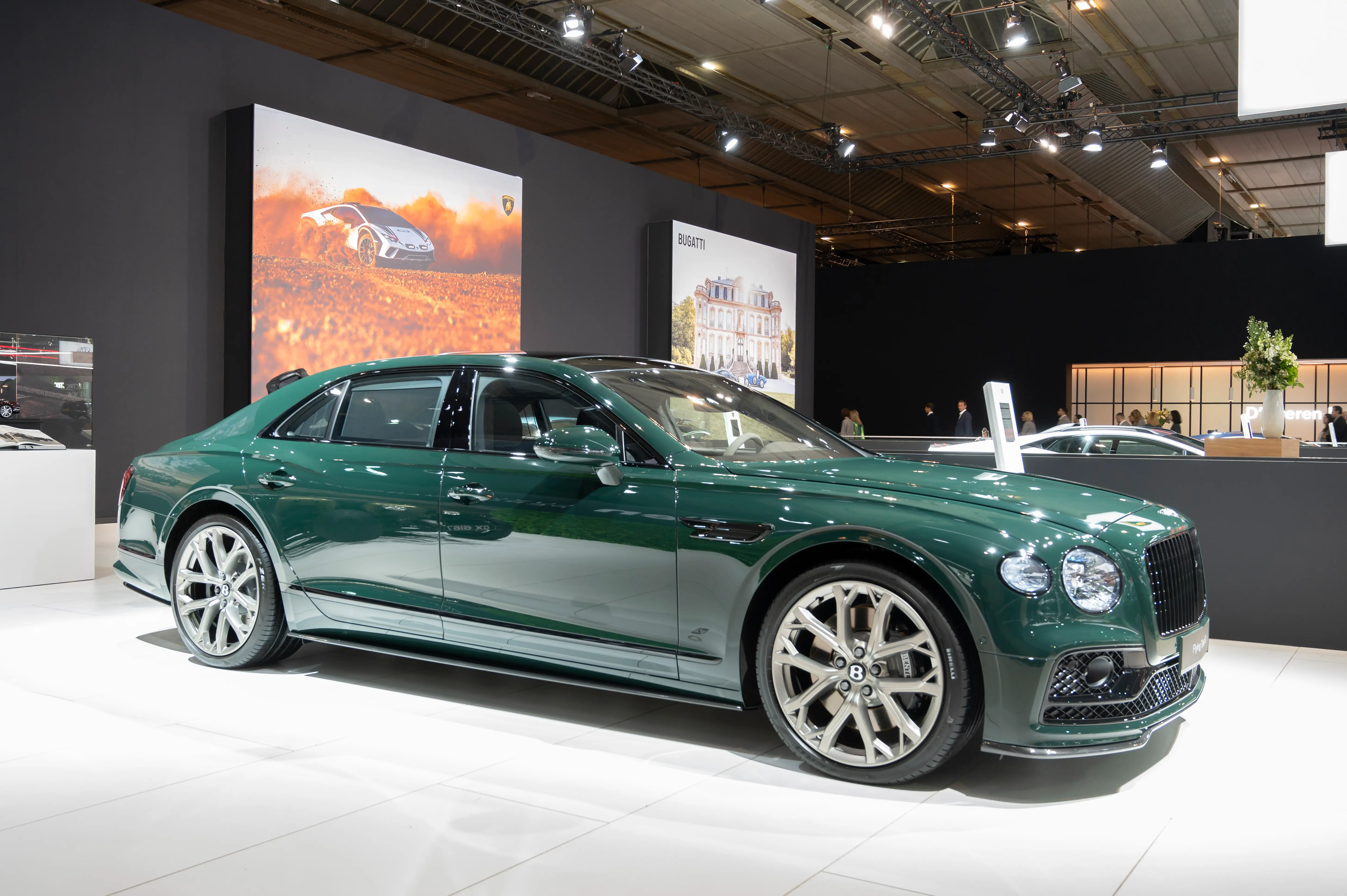 A green Bentley Flying Spur sedan is parked on a white tile showroom floor.