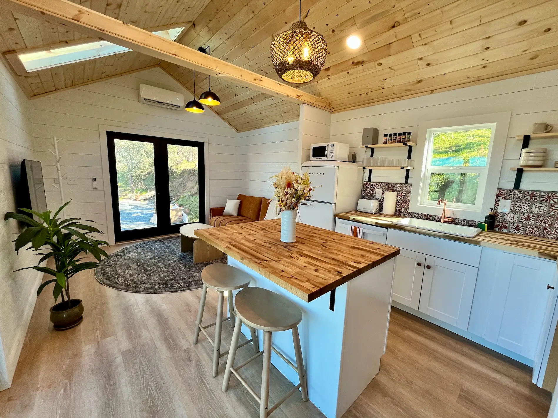 A warm-toned kitchen in a tiny home with an island and a farmhouse sink.