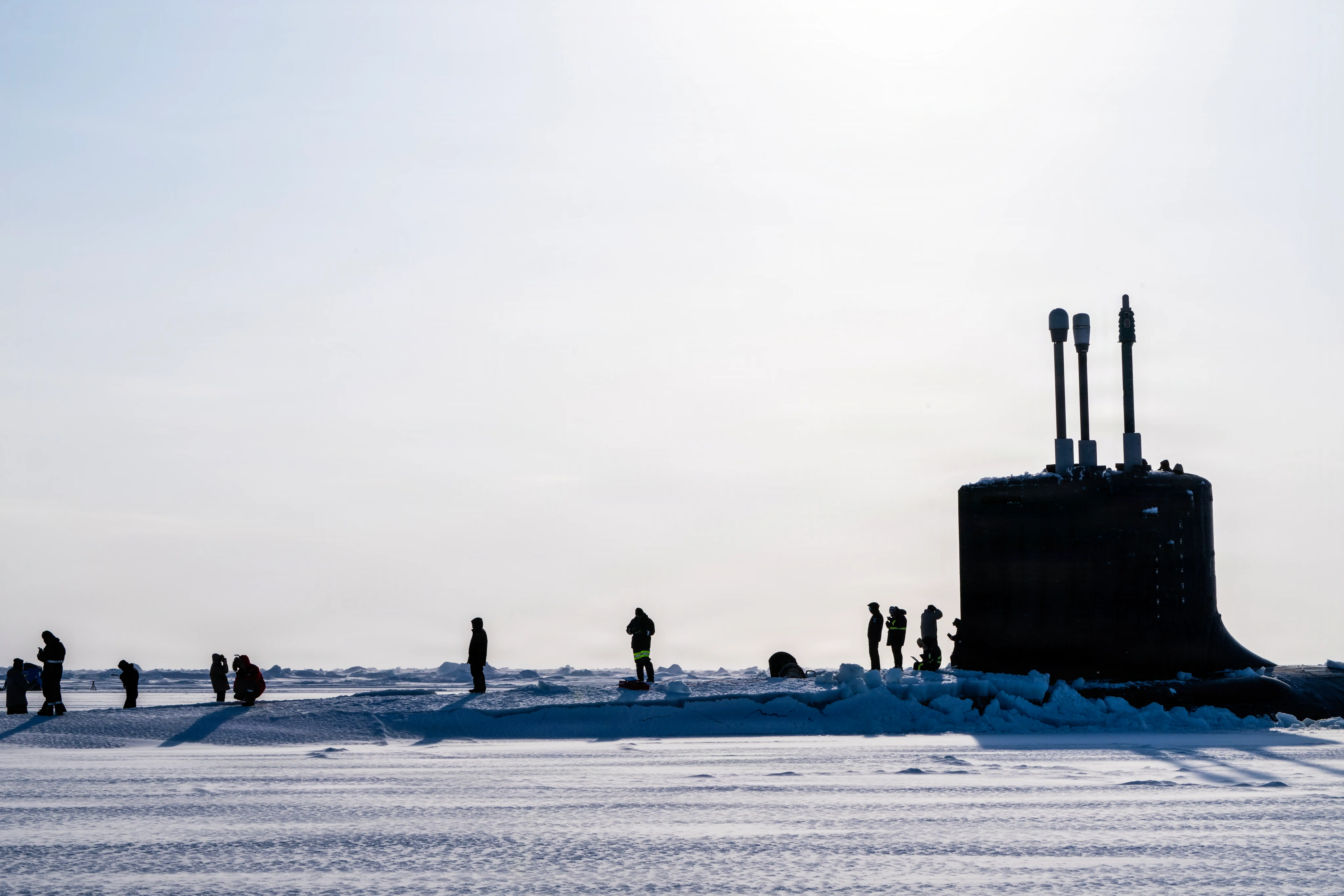 A Virginia-class submarine sits in ice with people standing on top of it.