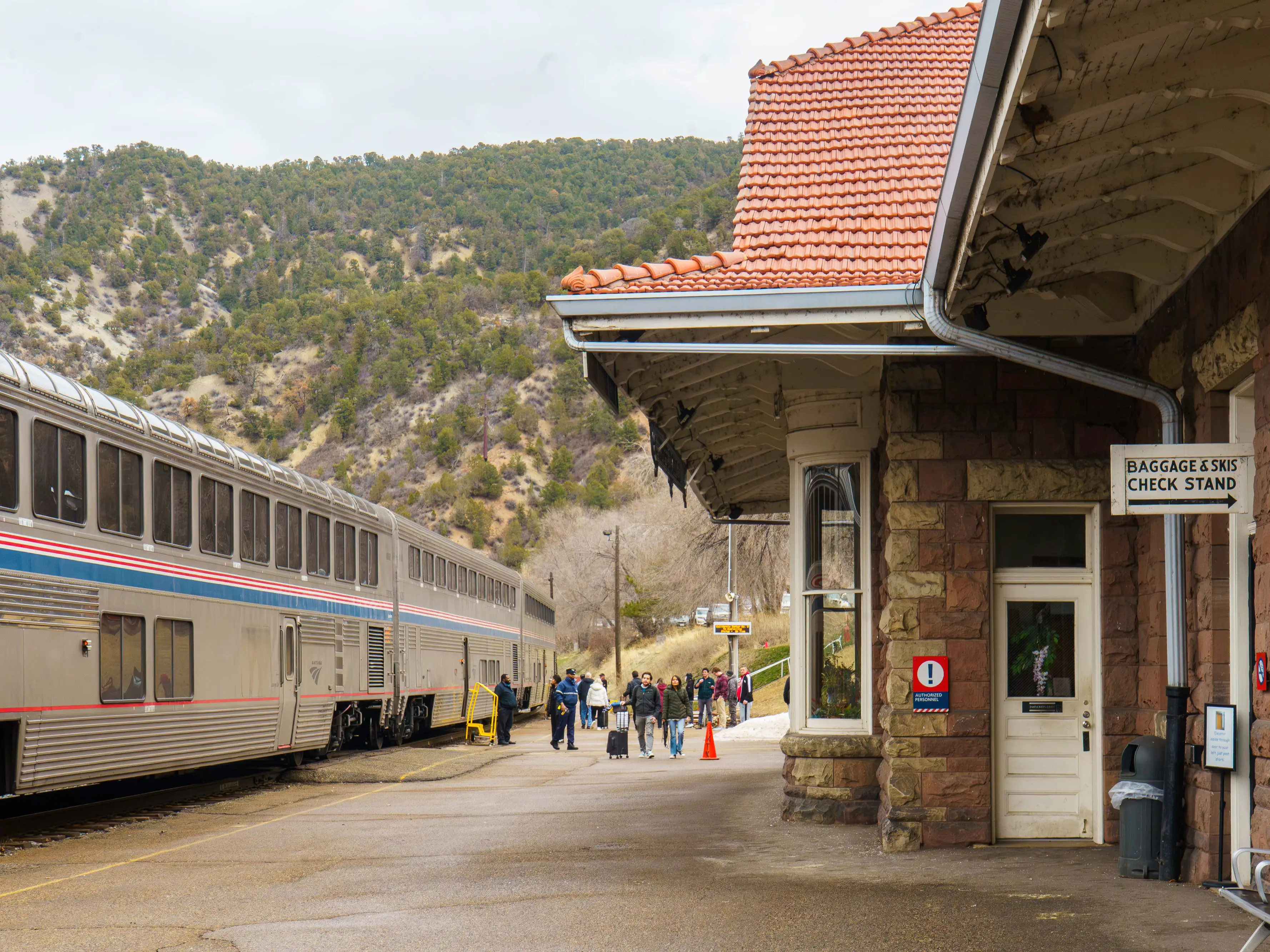 An Amtrak train parked at an outdoor station with mountains in the background