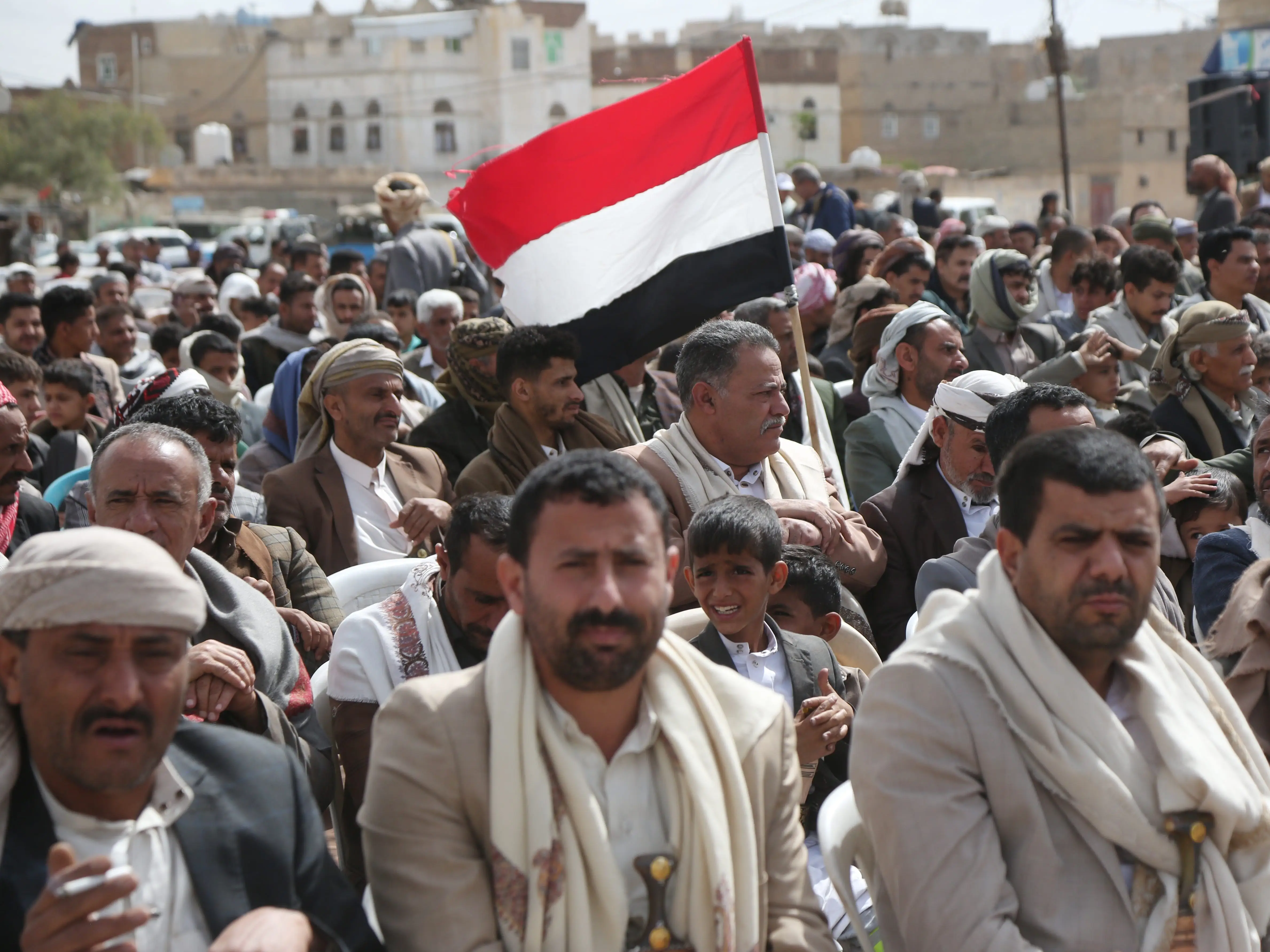 People in Yemen march with a Yemeni flag.
