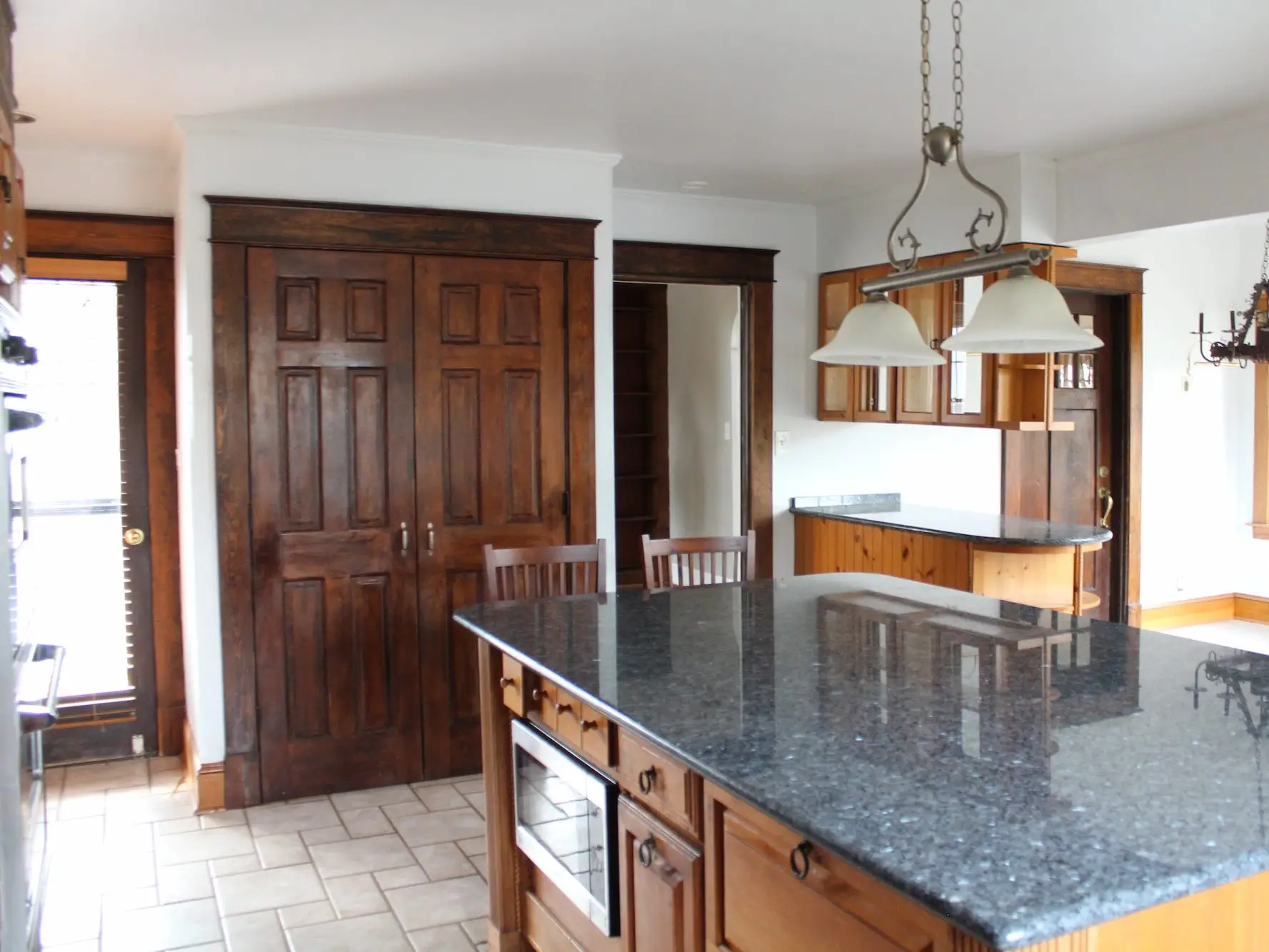 A kitchen with a large island wooden doors that lead to a pantry.