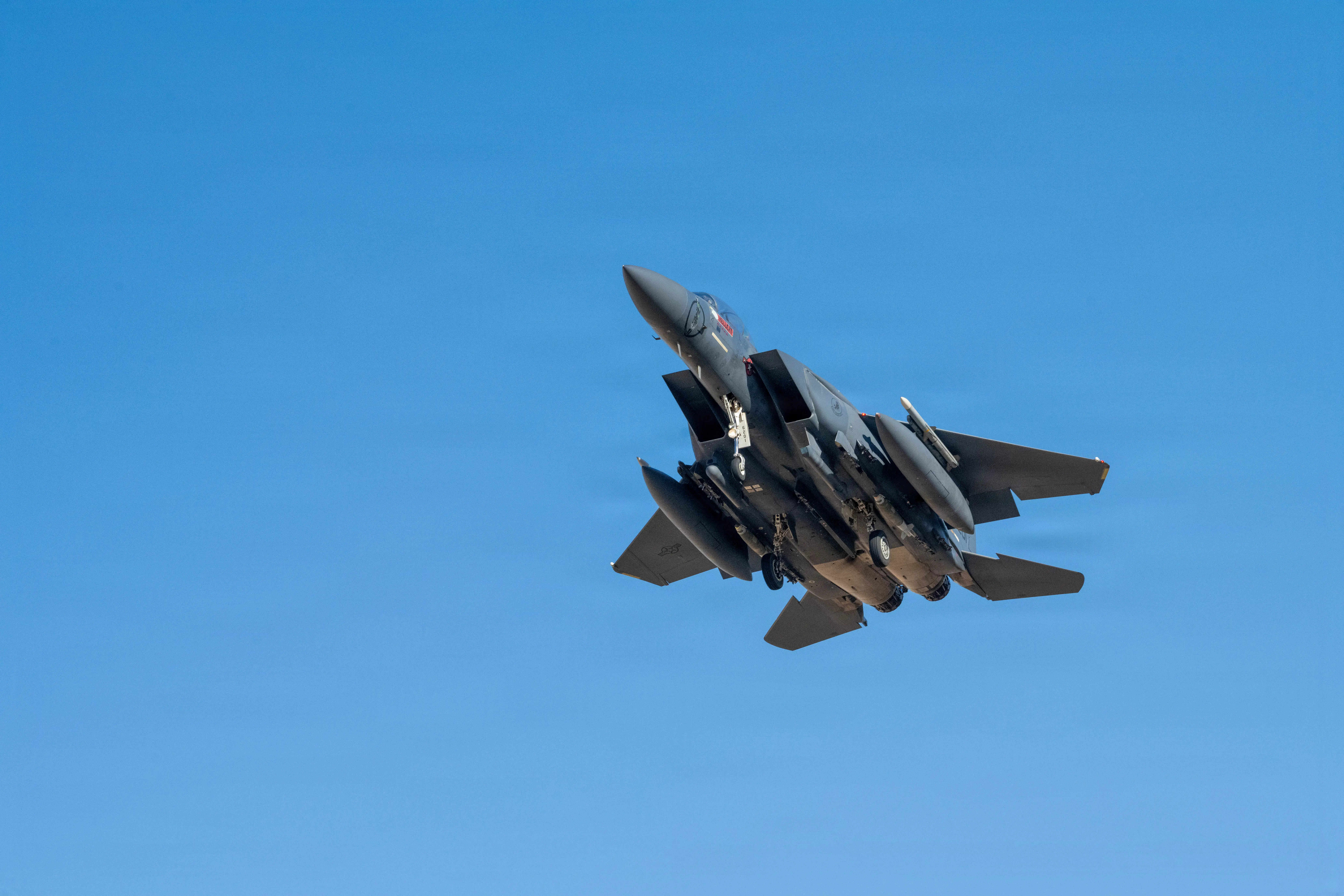 A US Air Force F-15 fighter flies in clear blue sky.