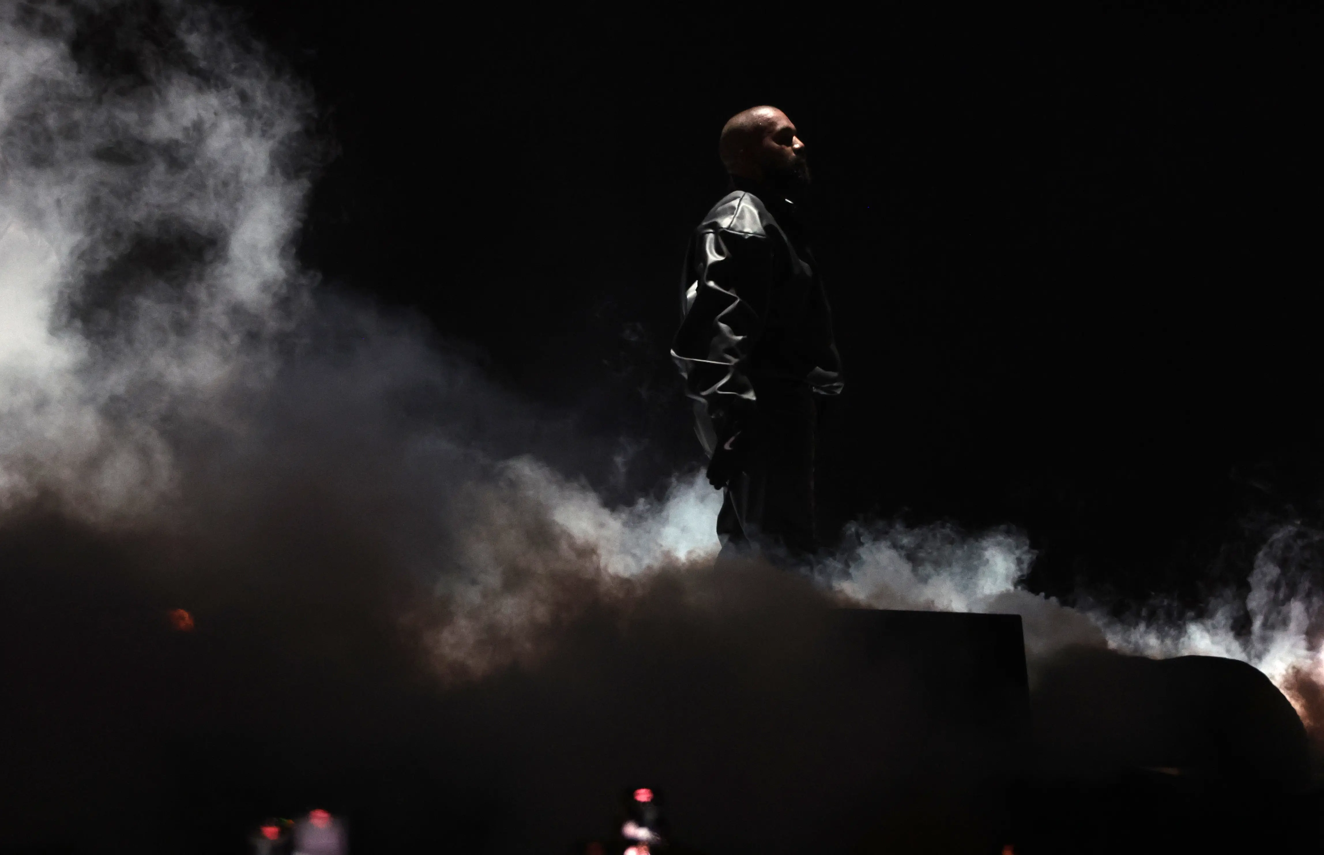 Kanye West in side profile standing on a smoky stage.