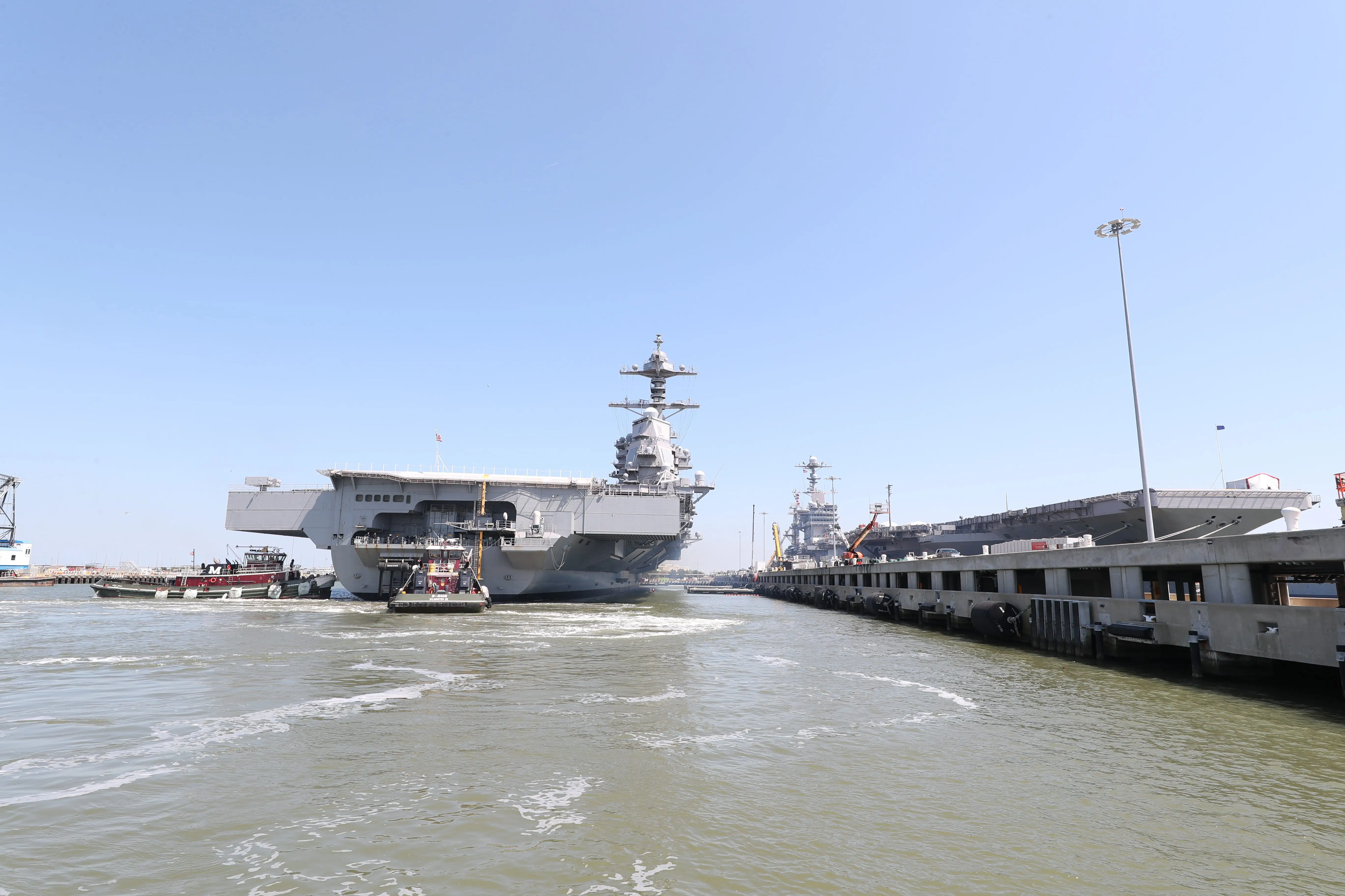 An aircraft carrier sits in water at a shipyard.